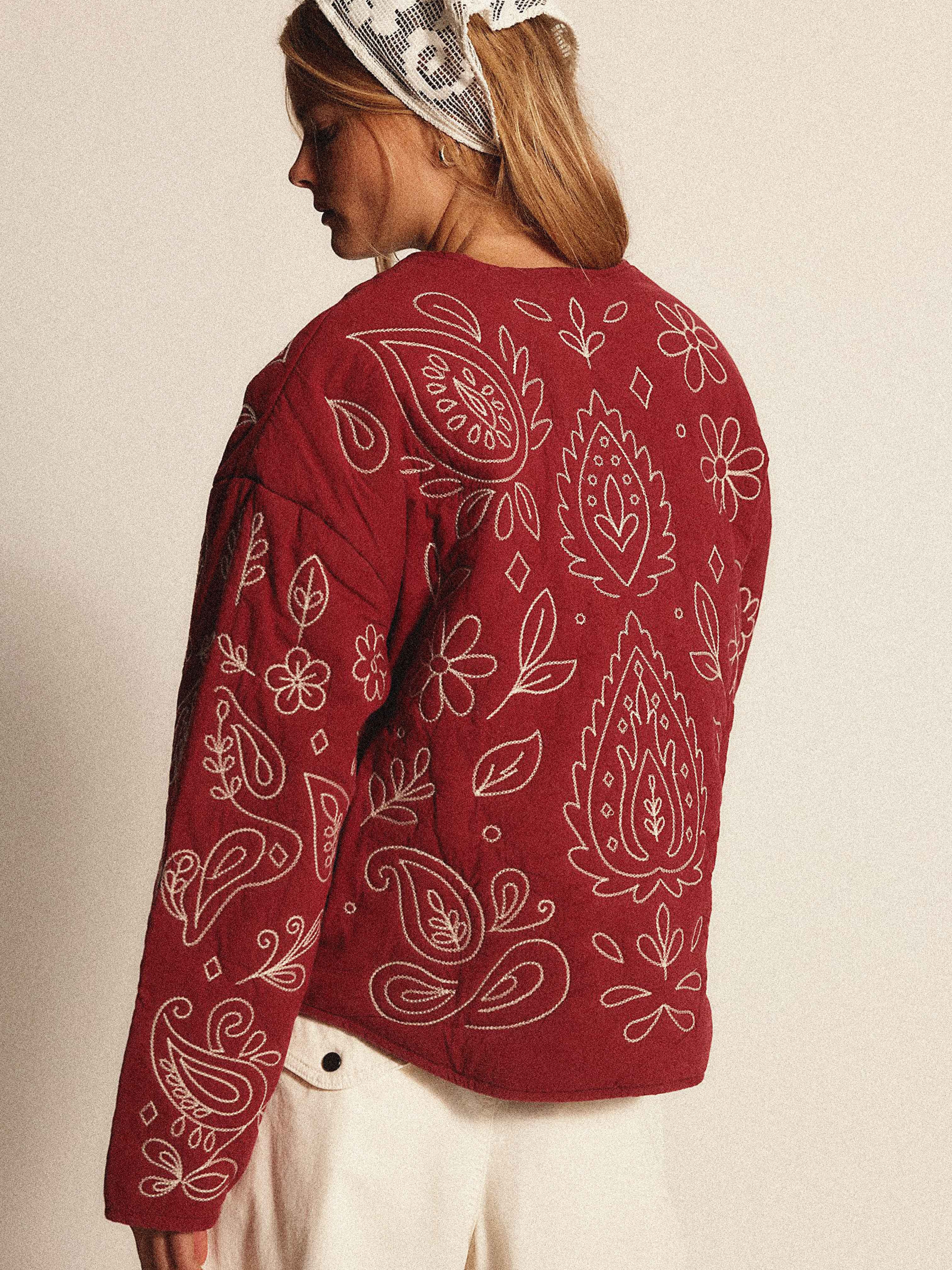 Back view of a woman wearing a burgundy quilted jacket with cream bandana-inspired embroidery.