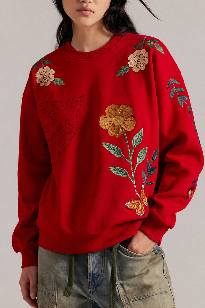 Person wearing a red sweatshirt with embroidered flowers, a hummingbird, and butterfly details.