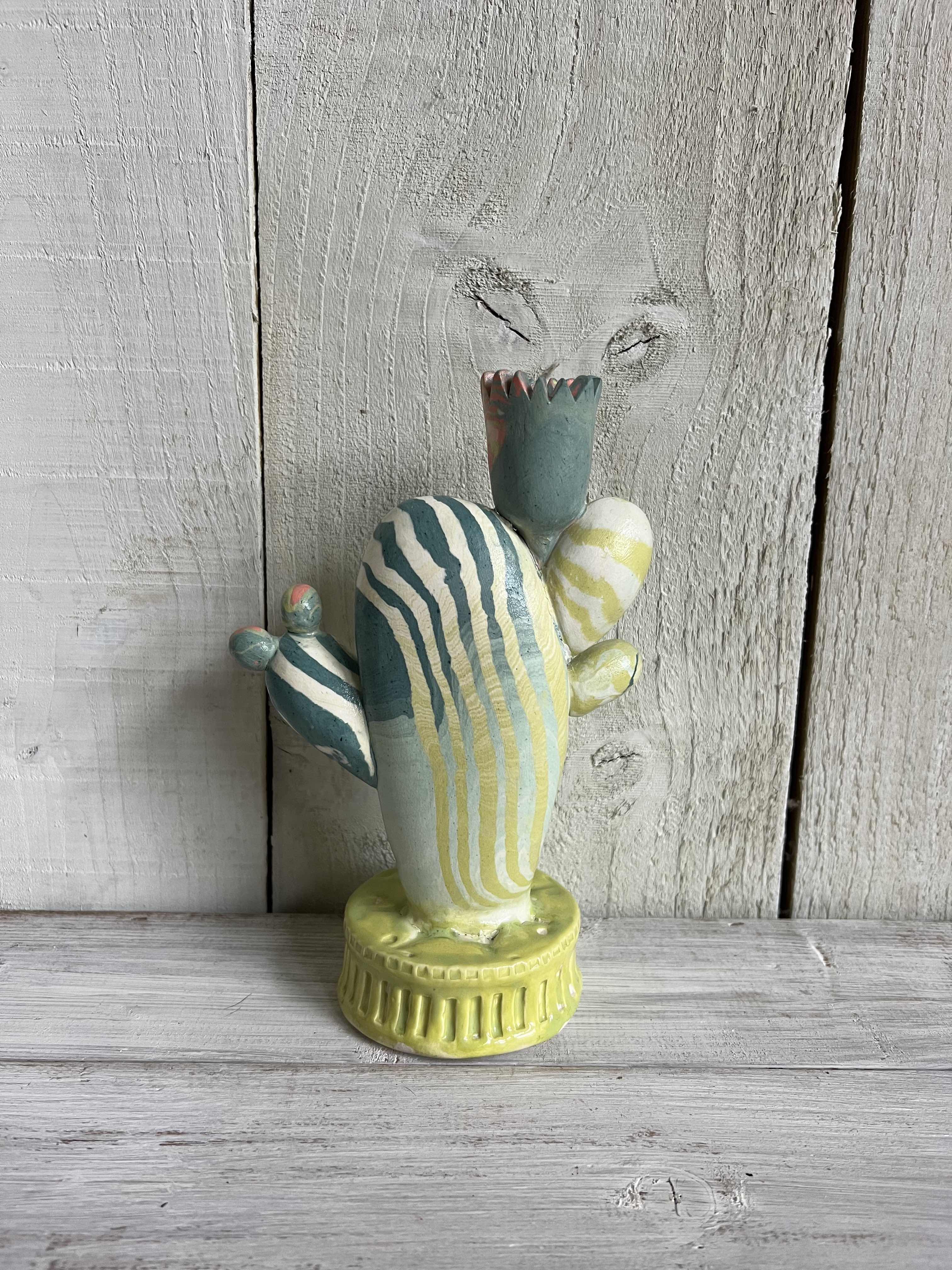 Handmade nerikomi ceramic cactus candle holder with striped clay pattern and coral flower details displayed on a rustic wooden shelf.