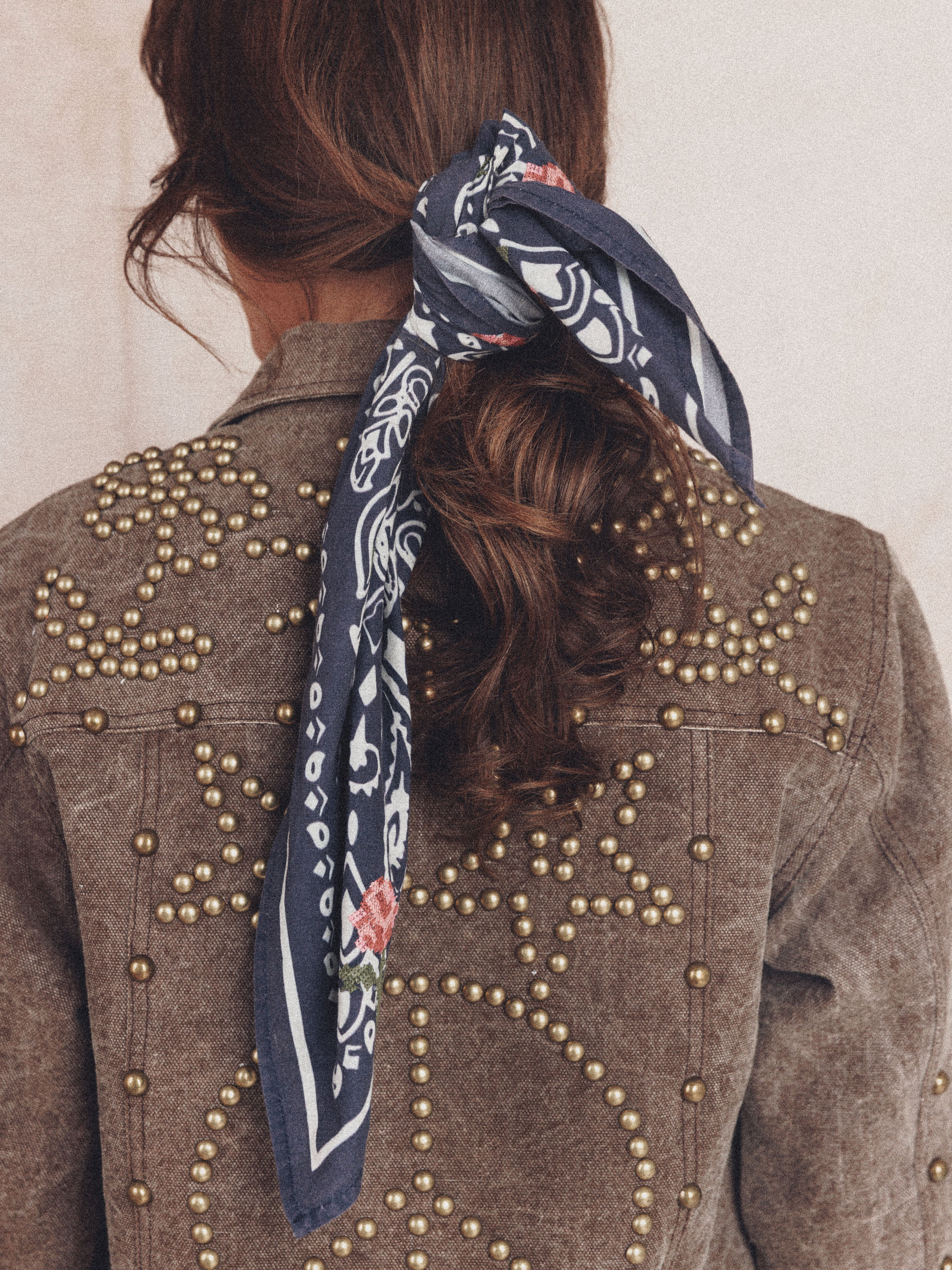 Woman wearing a navy bandana print scarf with rose embroidery tied around a low ponytail.
