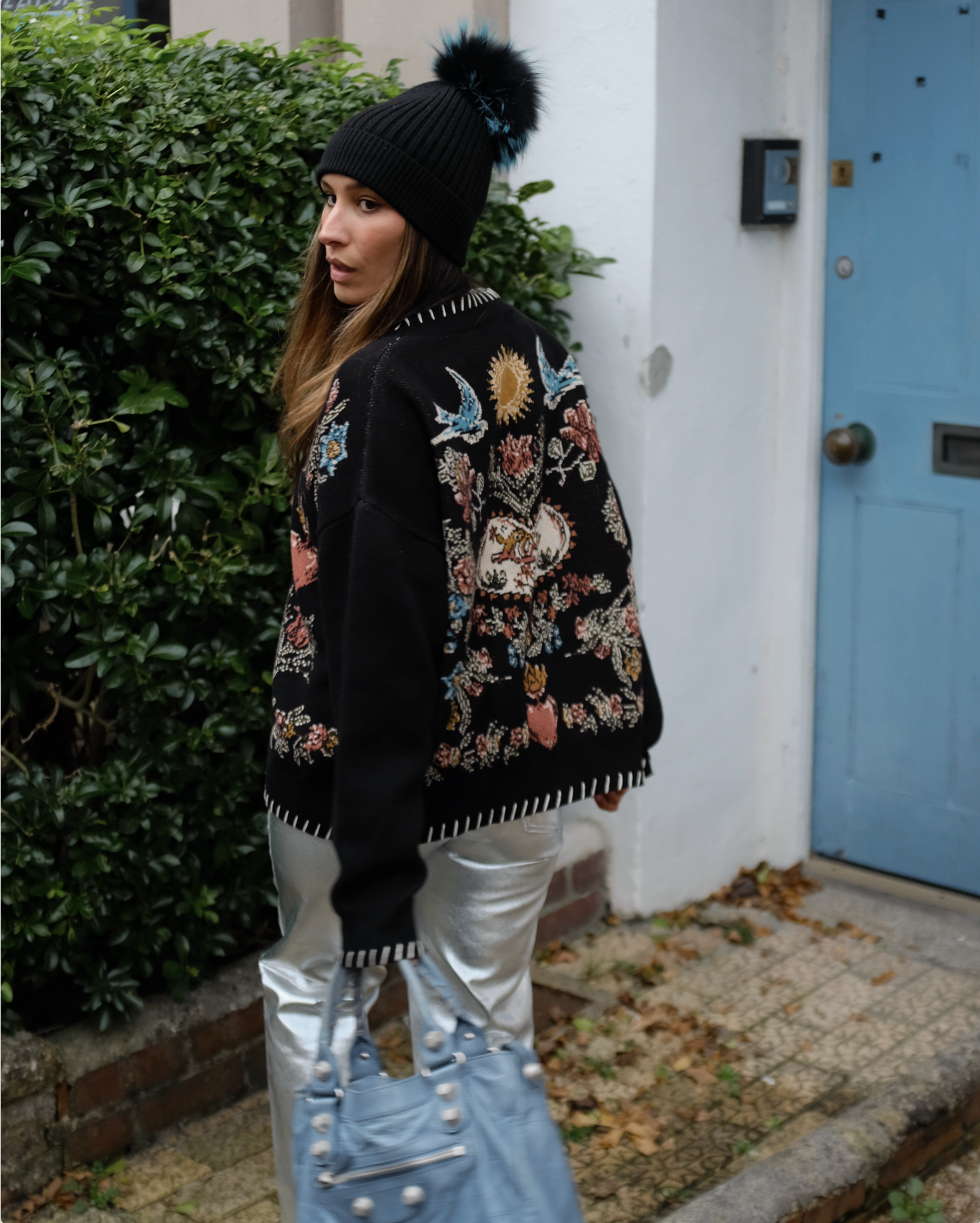 Back view of a person wearing a black knit cardigan featuring a heart, flowers, birds, and sun knit design.