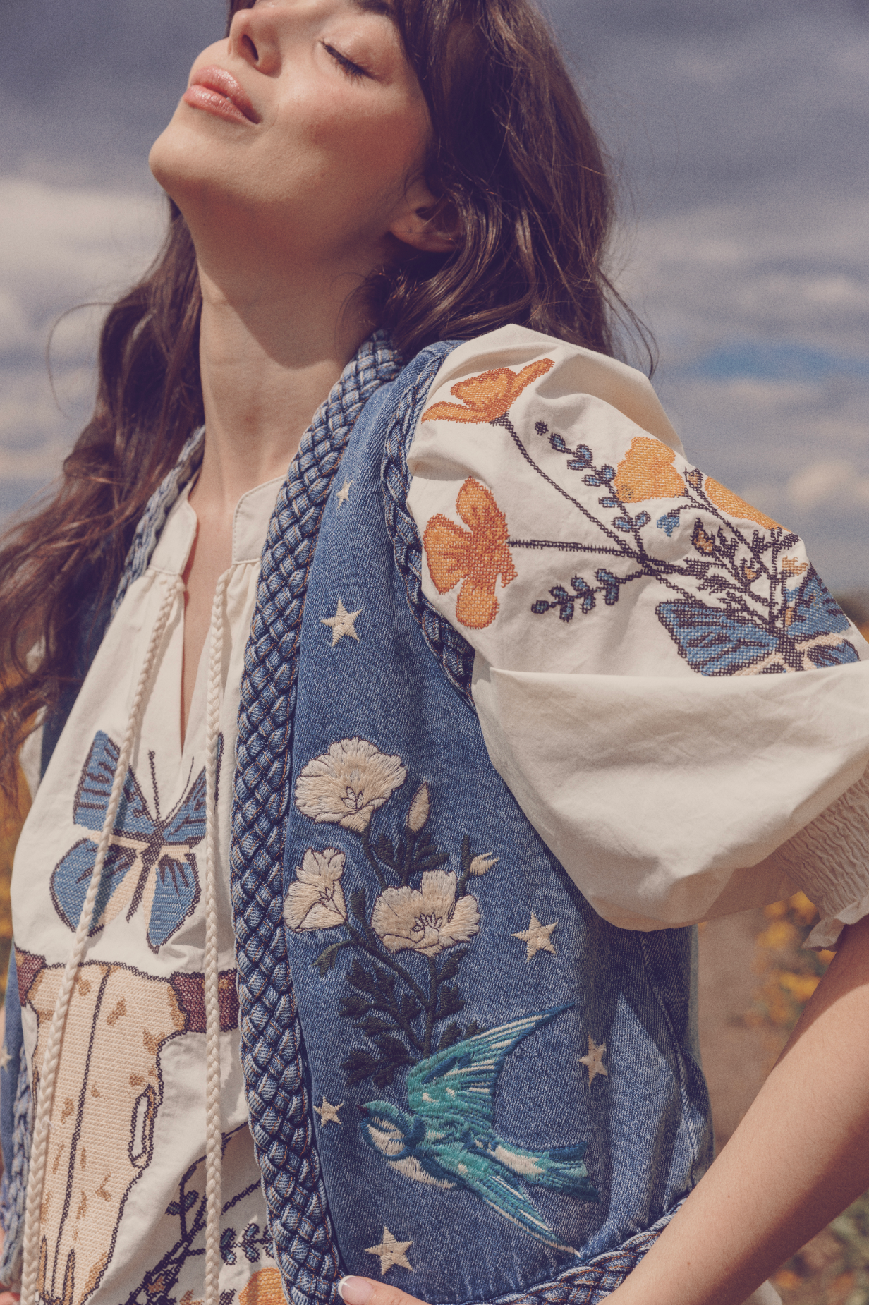 Front view of a person wearing a blue denim vest with white florals, birds and star embroidery details