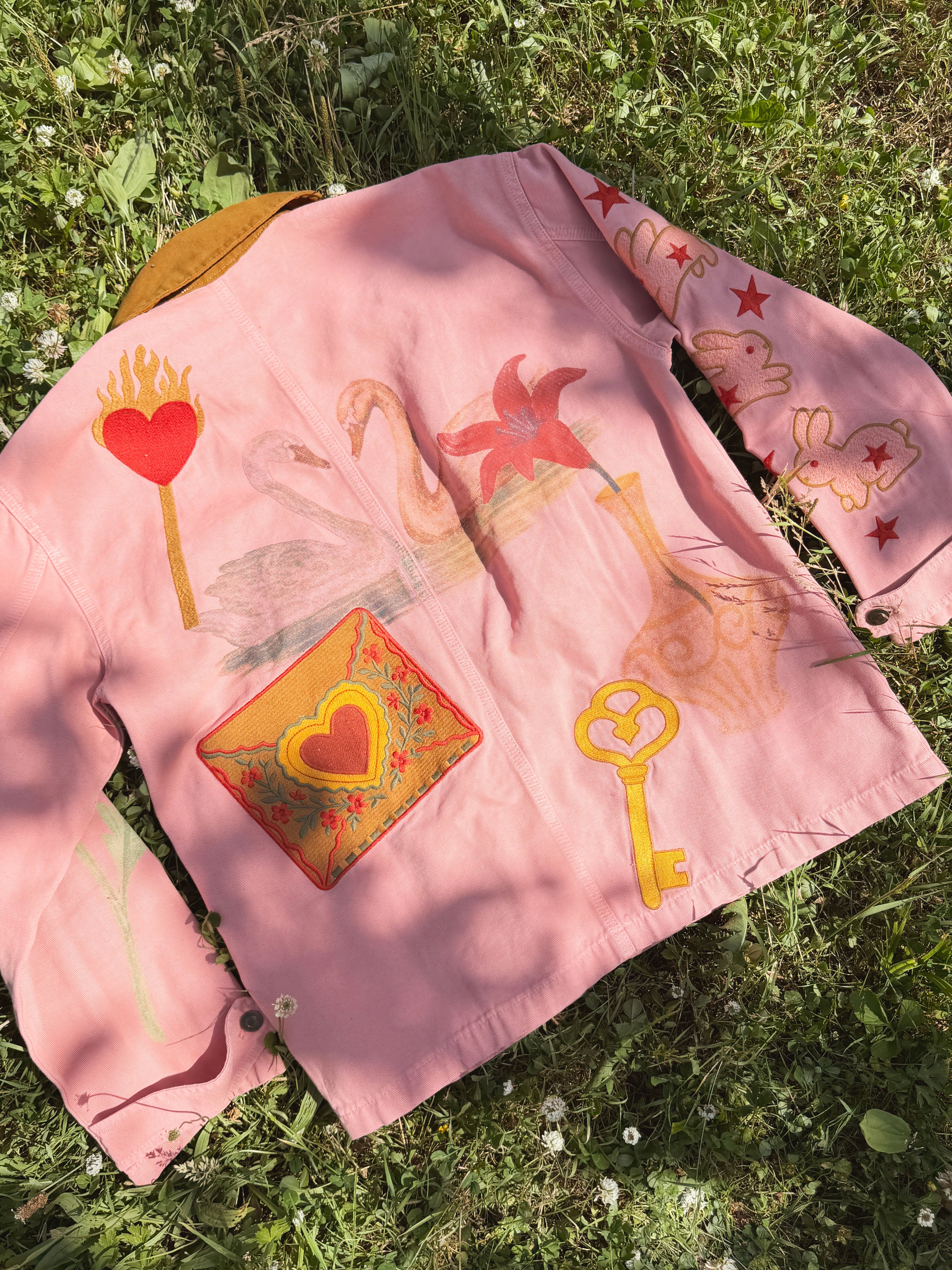 back view of a pink women's jacket with colourful hand-painted cherries, flowers, hearts, stars, and bunny illustrations.