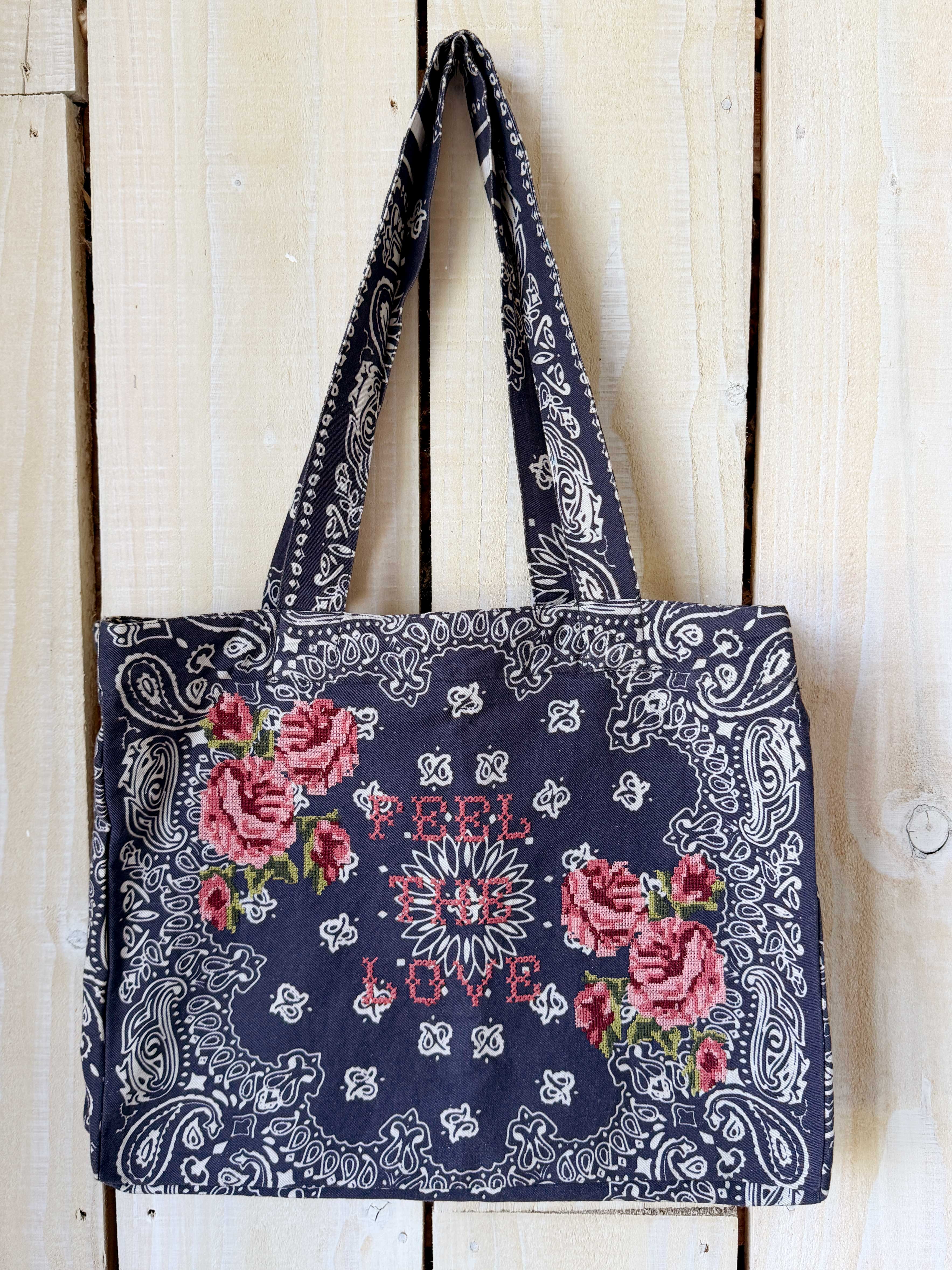 Navy bandana print canvas tote bag embroidered with cross stitch roses and the words "Feel the Love."
