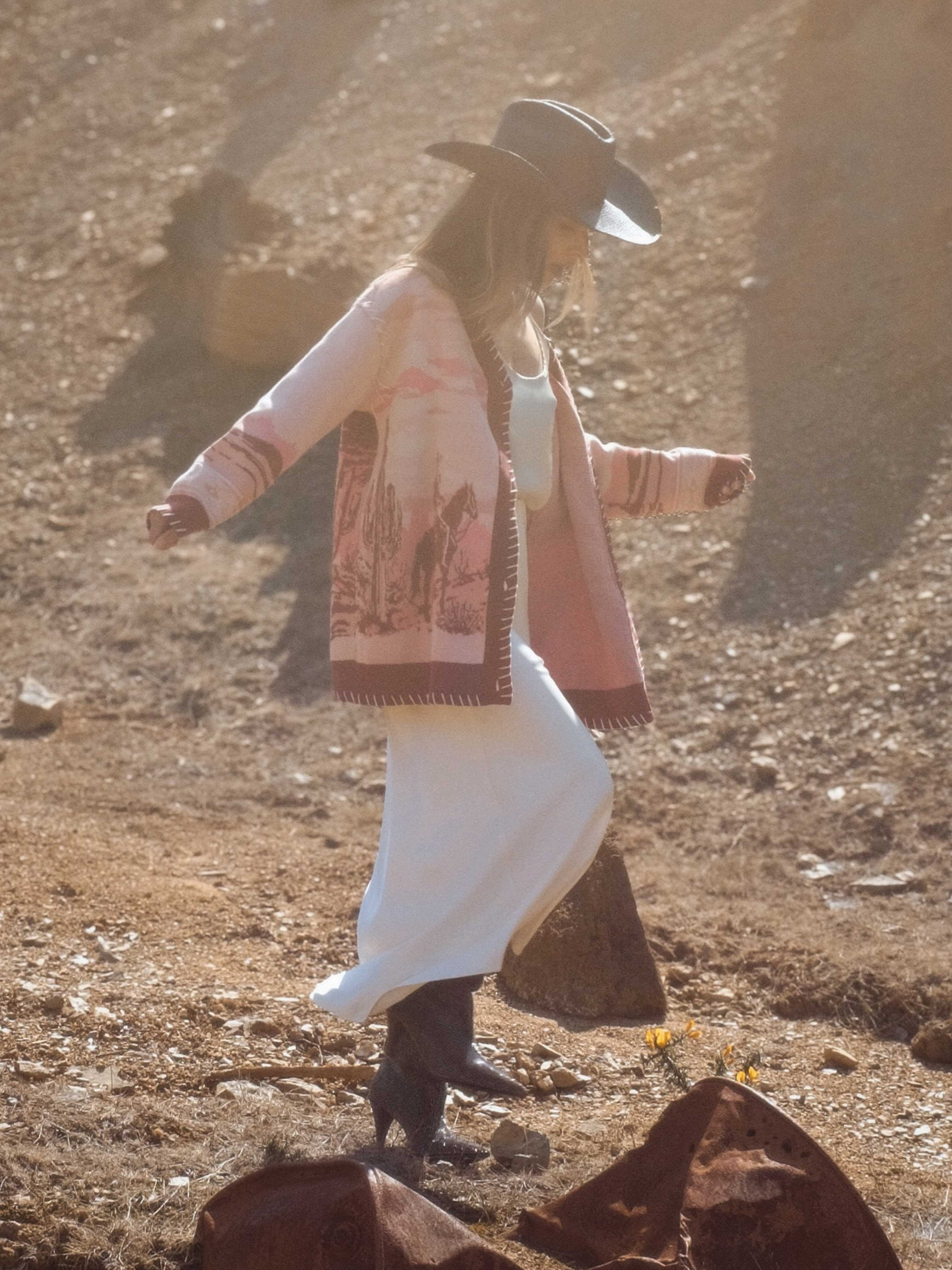 Person wearing a pink knit cardigan with a western desert landscape knit pattern featuring horses and riders.