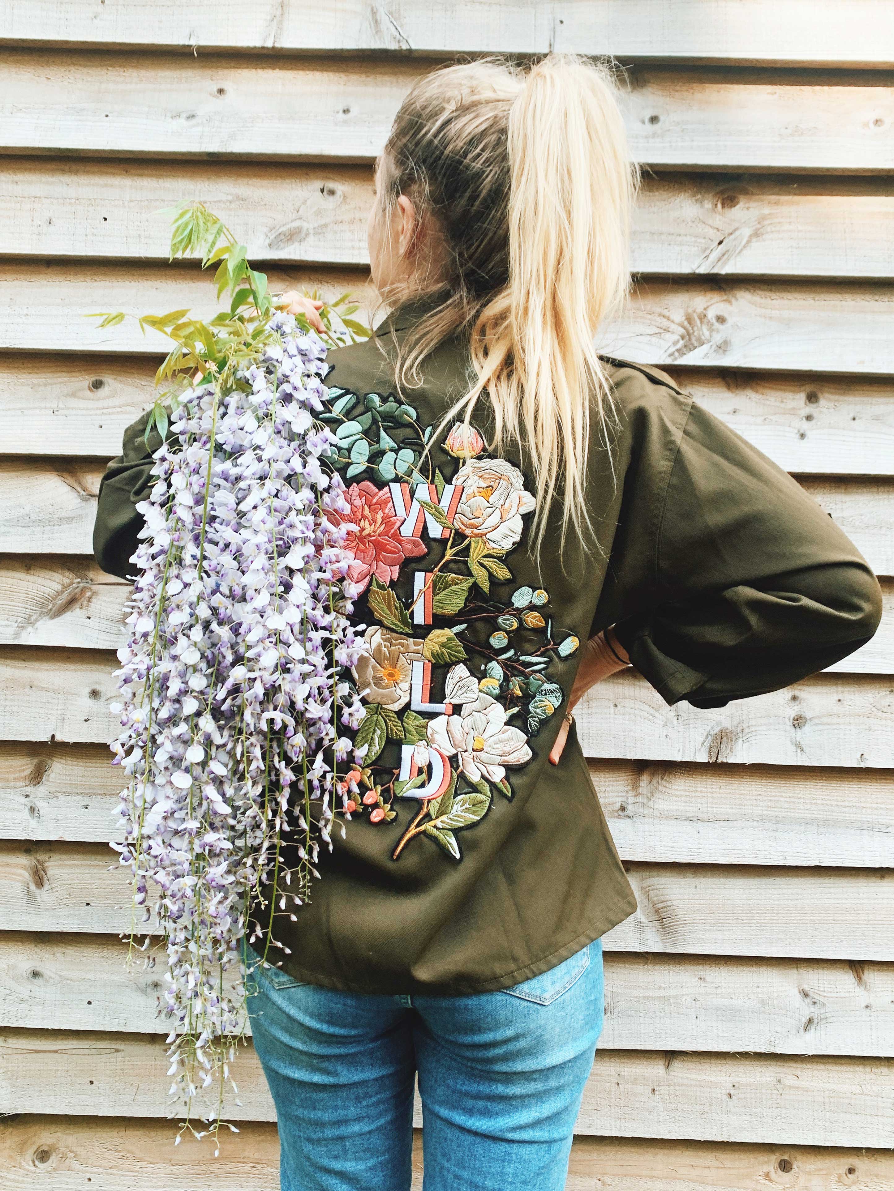 Olive green jacket with colourful floral embroidered back design and "WILD" lettering, back view.