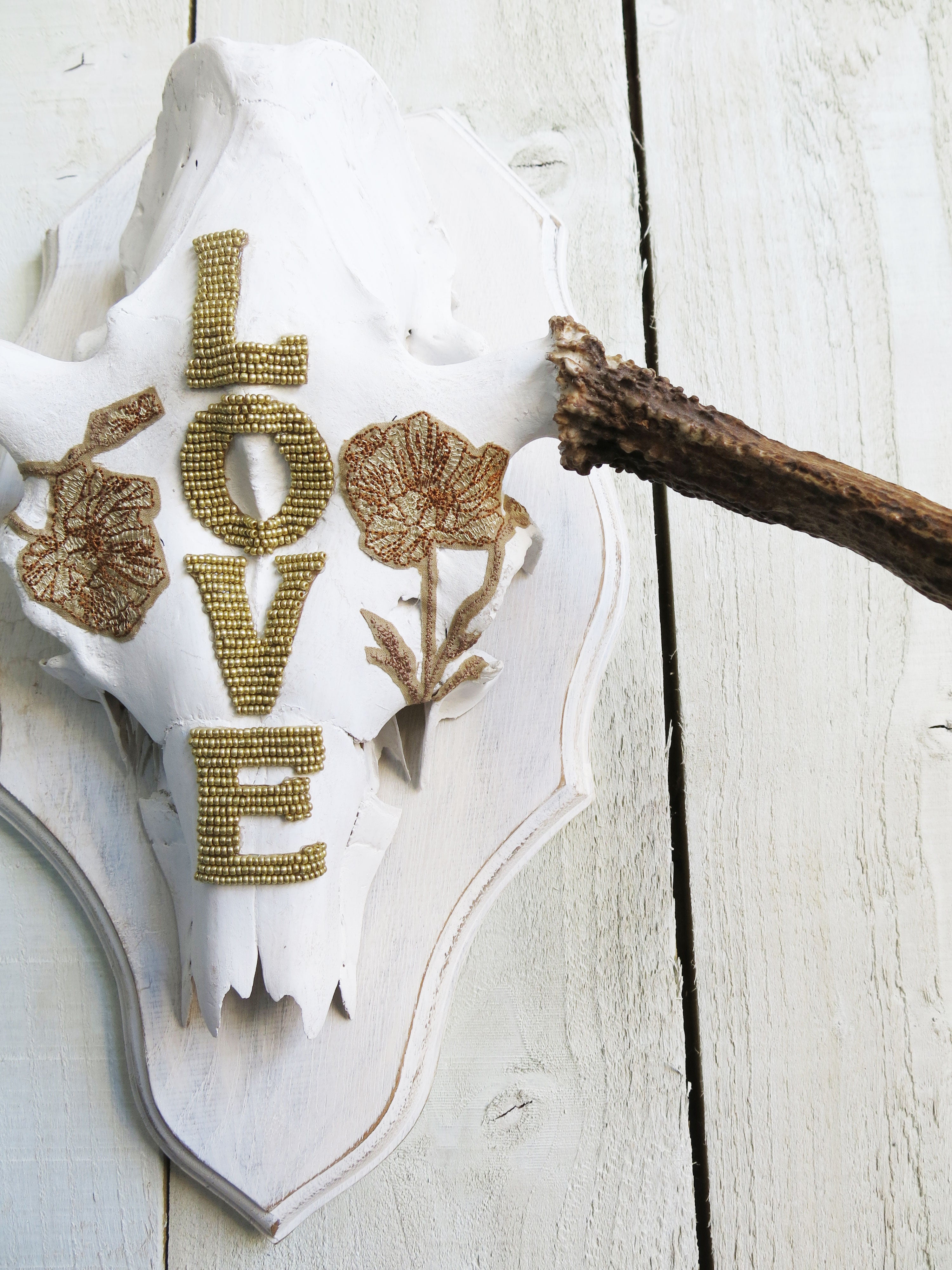 Handcrafted moose skull wall décor with natural antlers, gold beaded lettering, and floral accents.