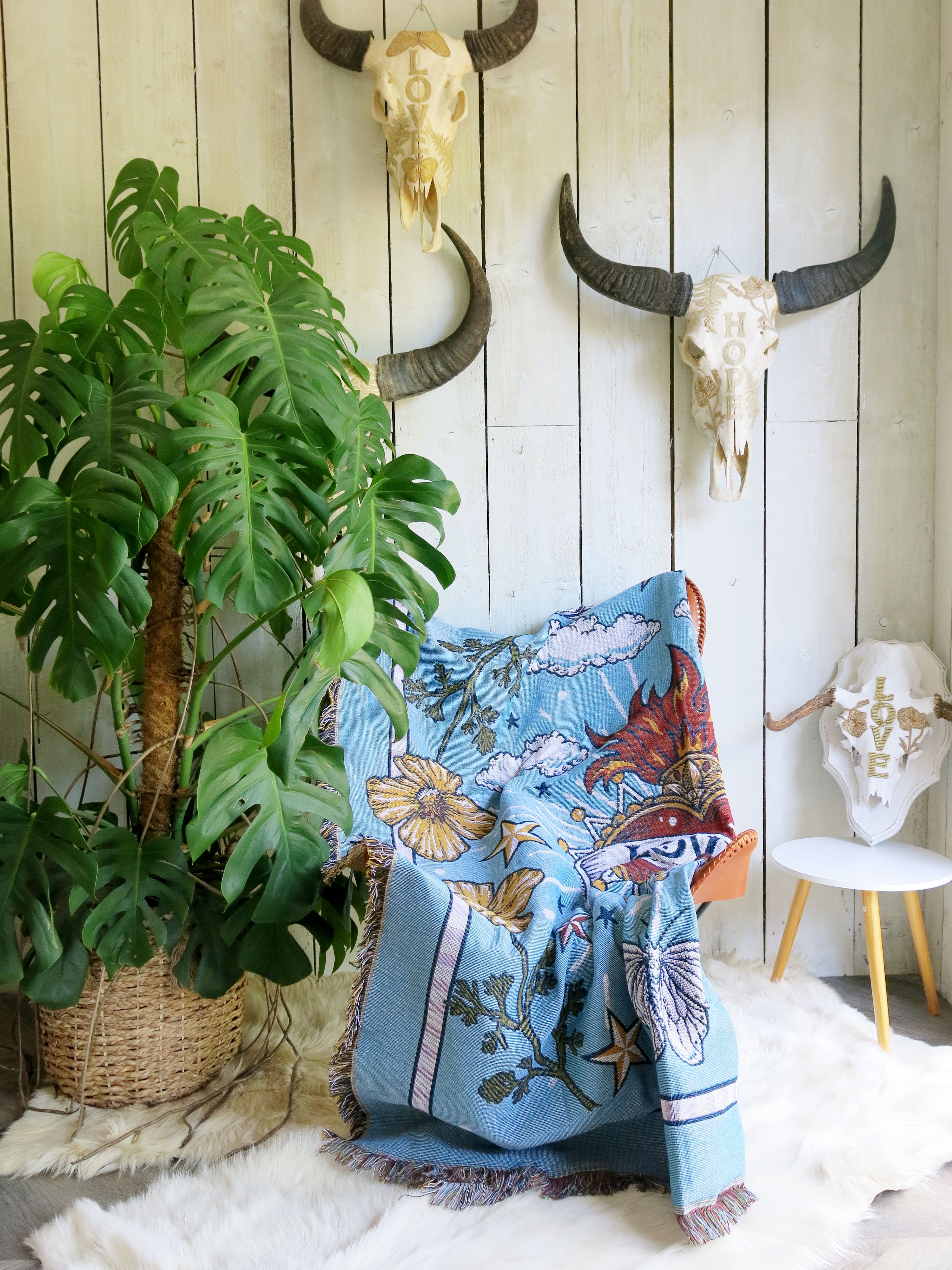 Light blue "Loved" woven throw blanket styled beside indoor plants in a cosy home interior.