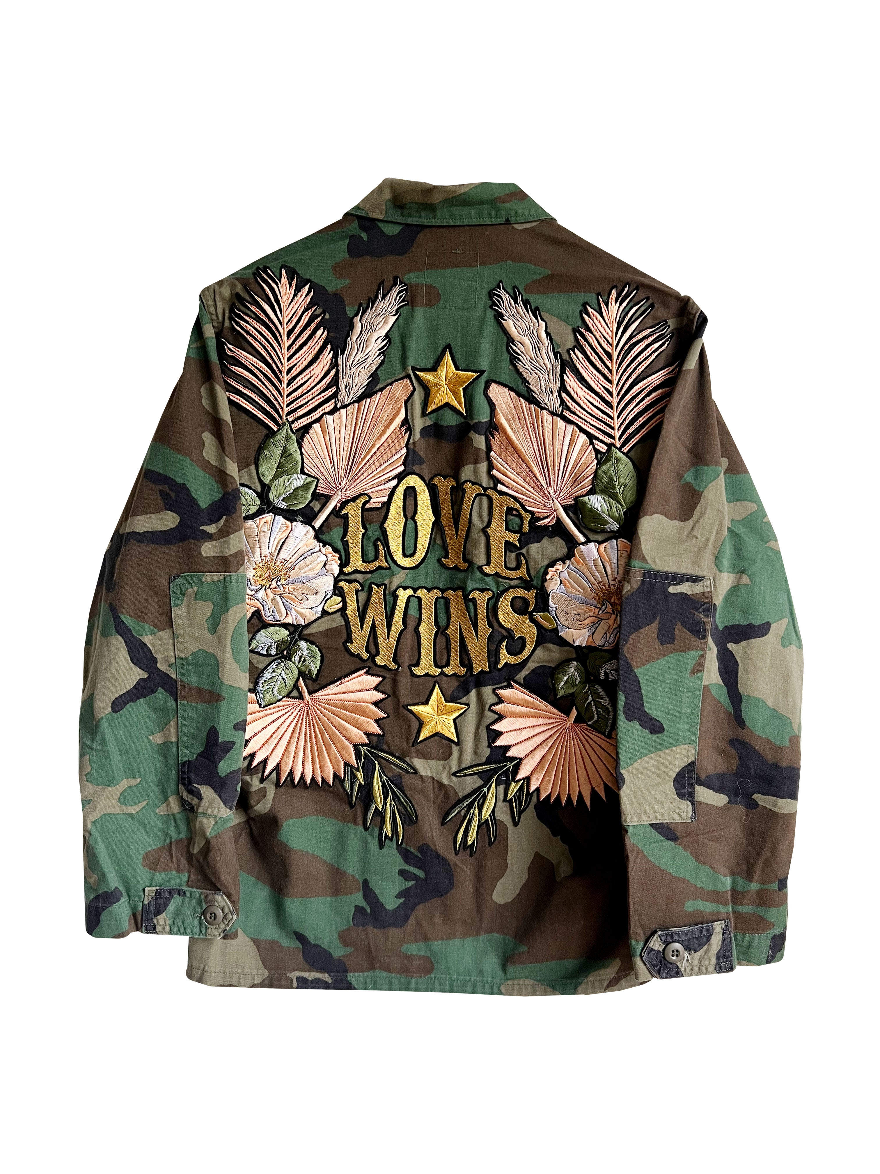 Back view of a camouflage military jacket with floral embroidered design and "LOVE WINS" lettering.