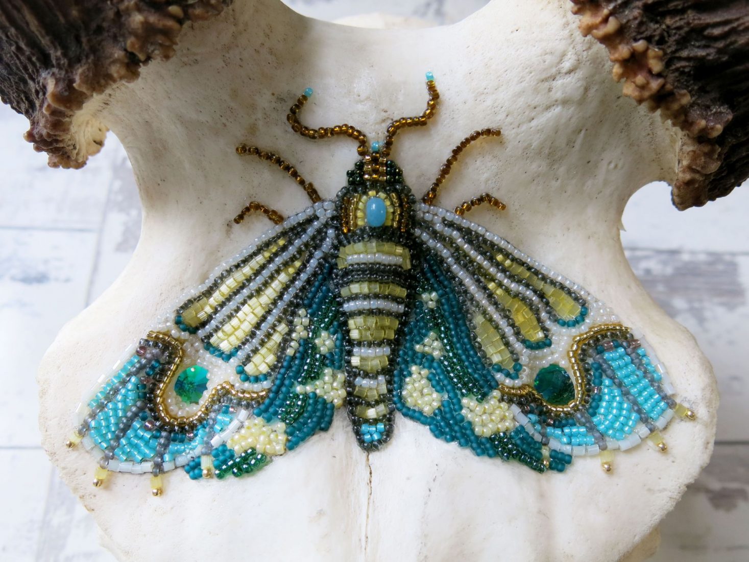 Close-up of a hand-beaded blue, turquoise, and gold moth embellishment on a decorative deer skull.