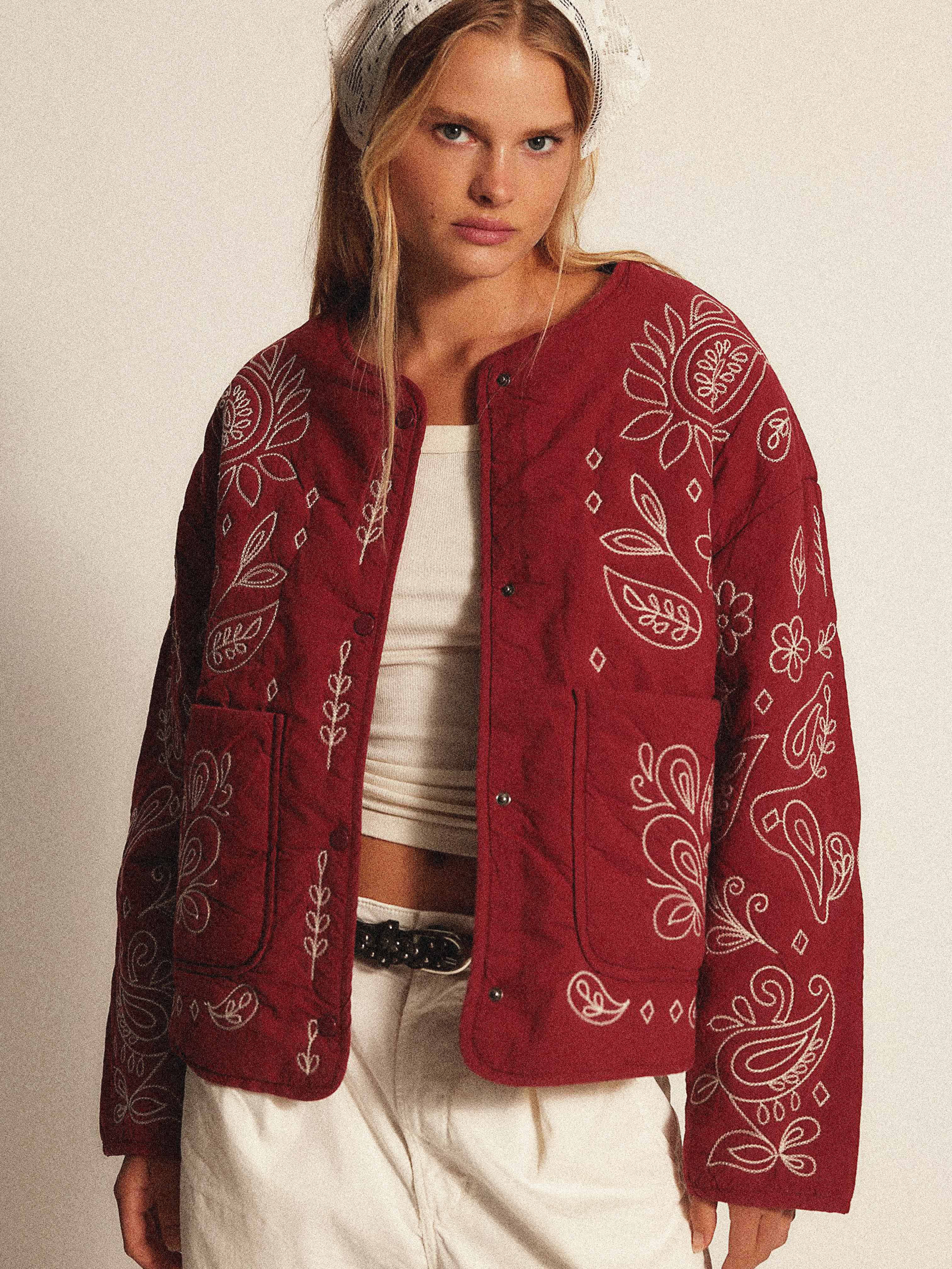 Woman wearing a burgundy quilted jacket with cream bandana-inspired embroidery.