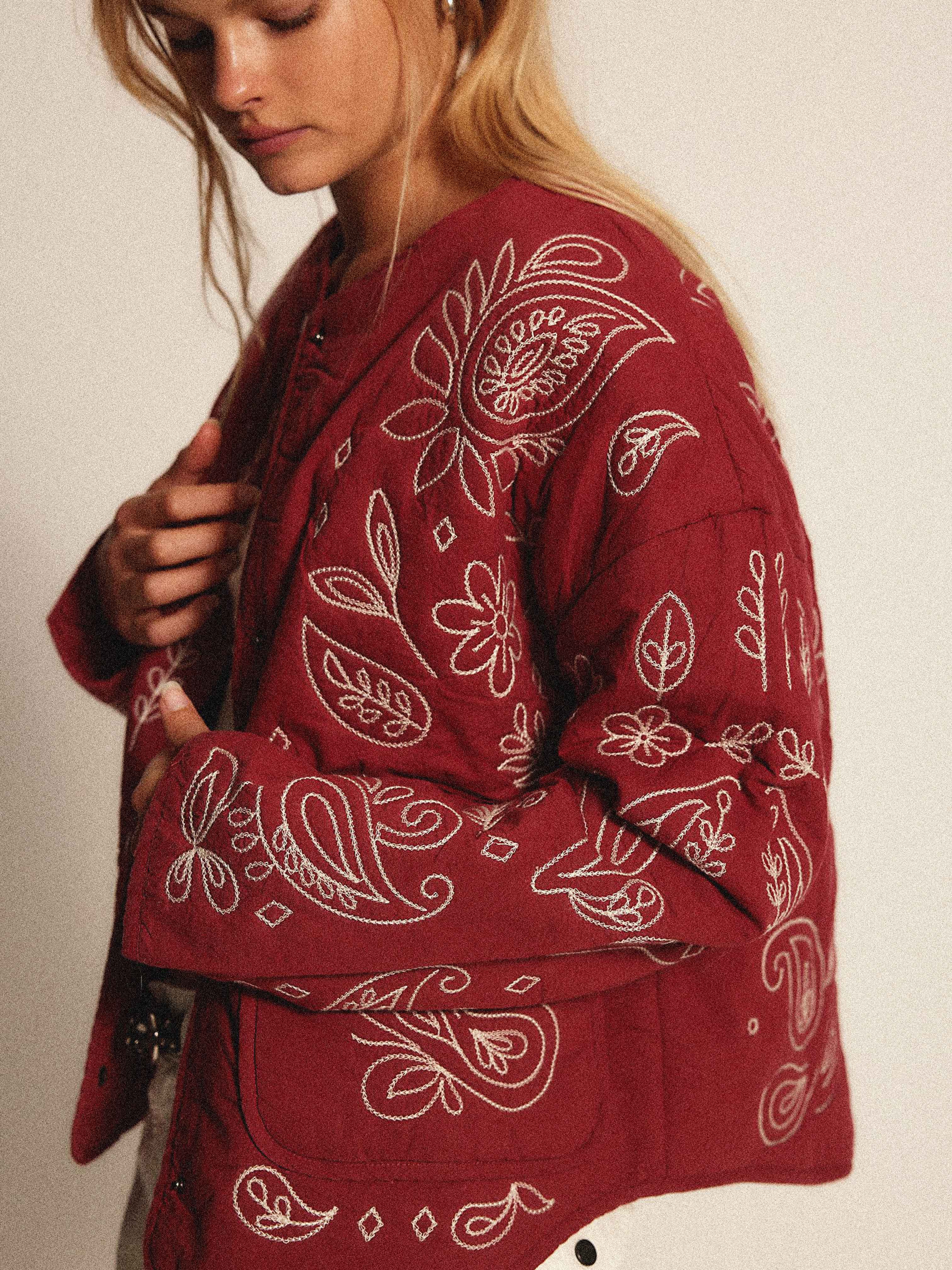 Woman wearing a burgundy quilted jacket with cream bandana-inspired embroidery.