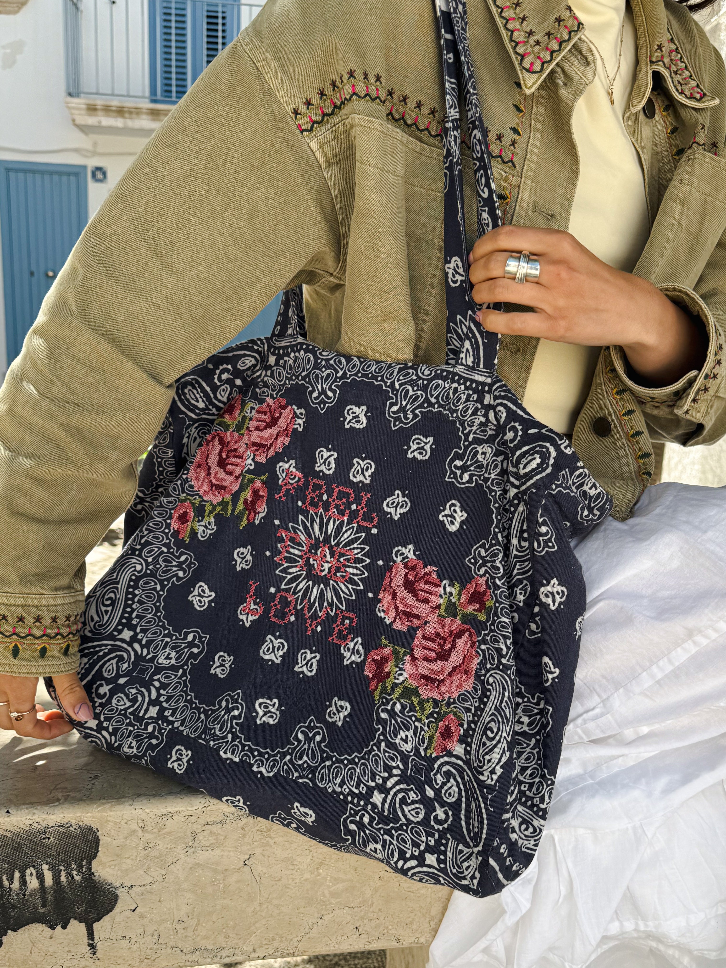 Close-up of a navy bandana print canvas tote bag embroidered with cross stitch roses and the words "Feel the Love."