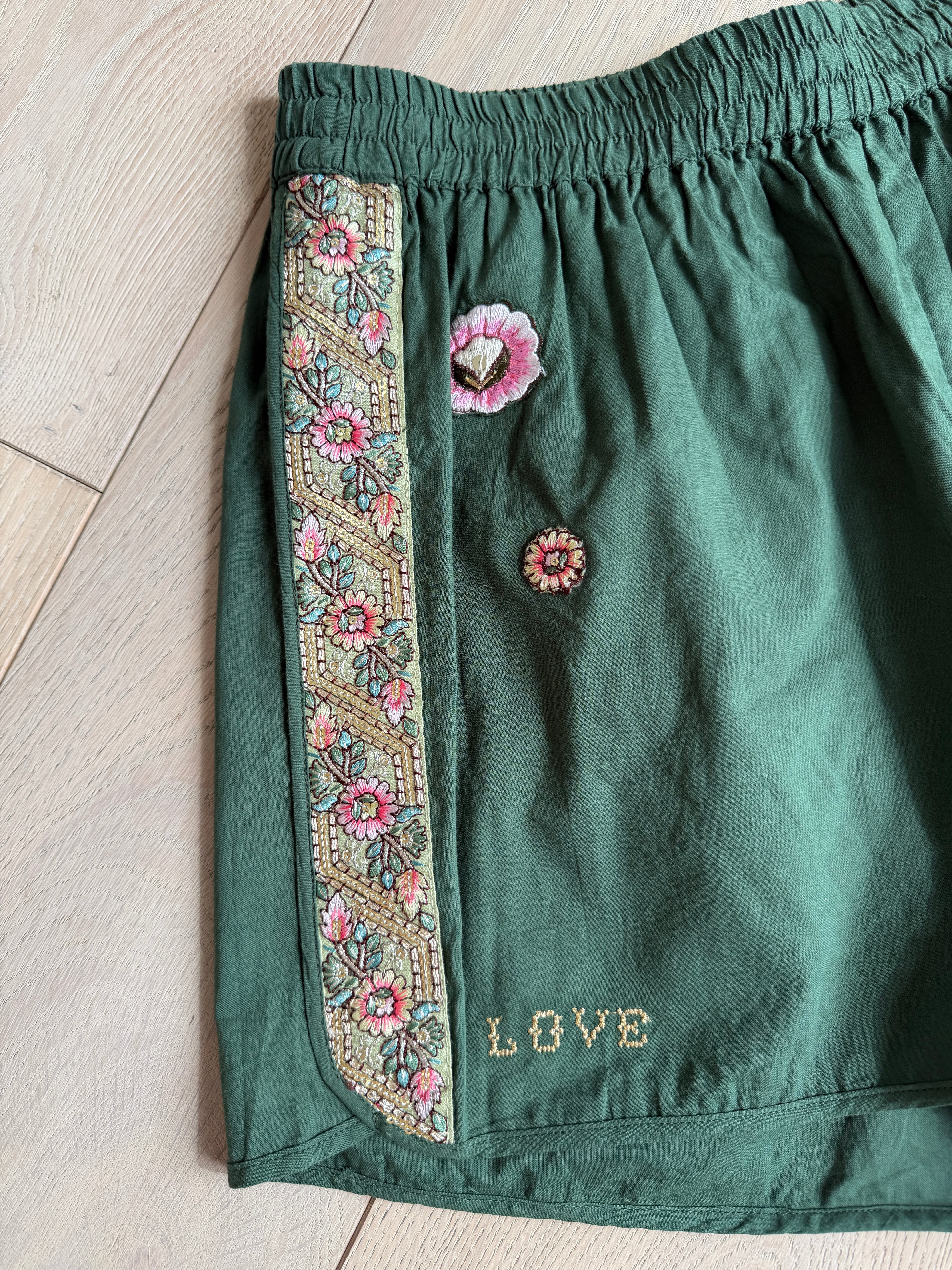 Green shorts with floral embroidered side trim, floral embroidered accents, elastic waistband, and embroidered "LOVE" text.