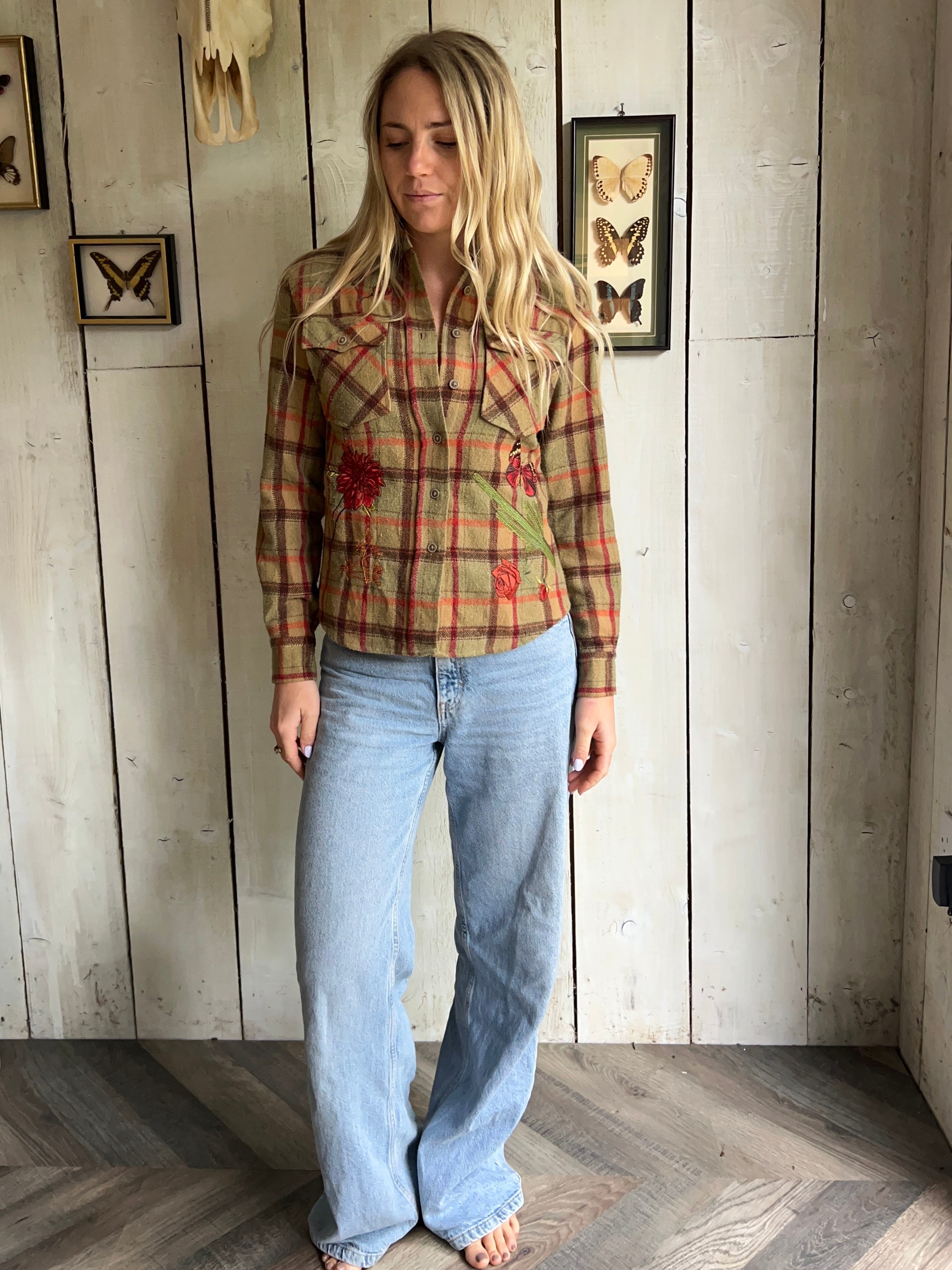 Person wearing a tan plaid shirt with red floral embroidery on the front.