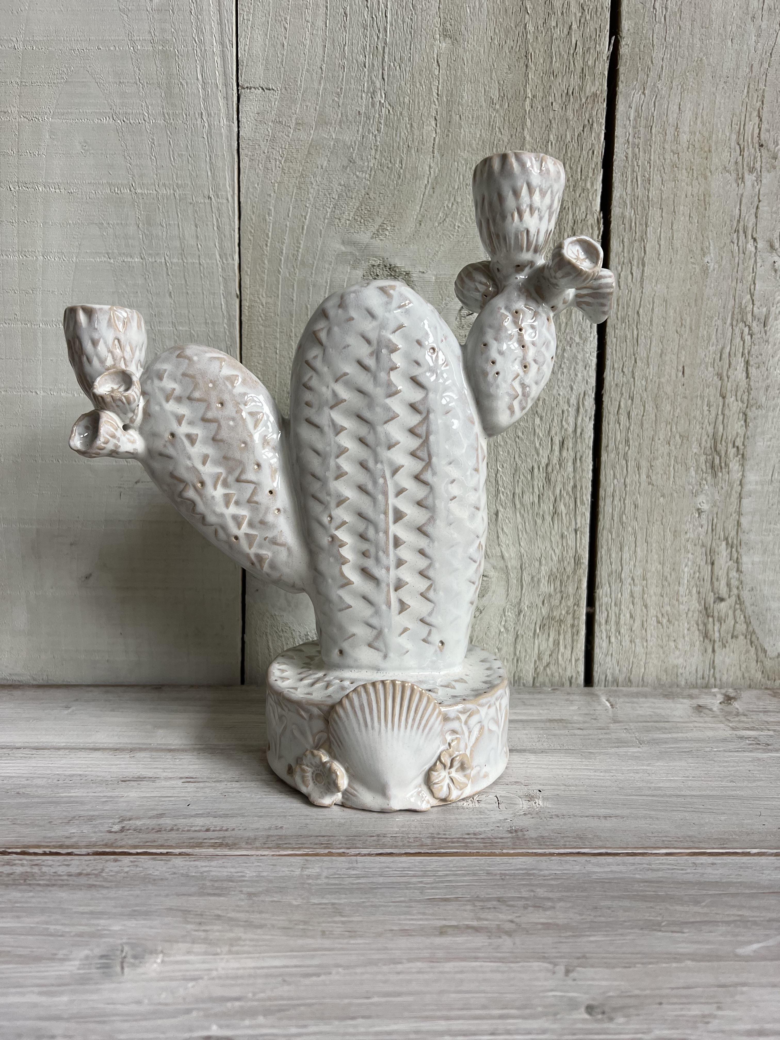Handmade white ceramic cactus candle holder with textured detailing and decorative shell base displayed on a rustic wooden shelf.