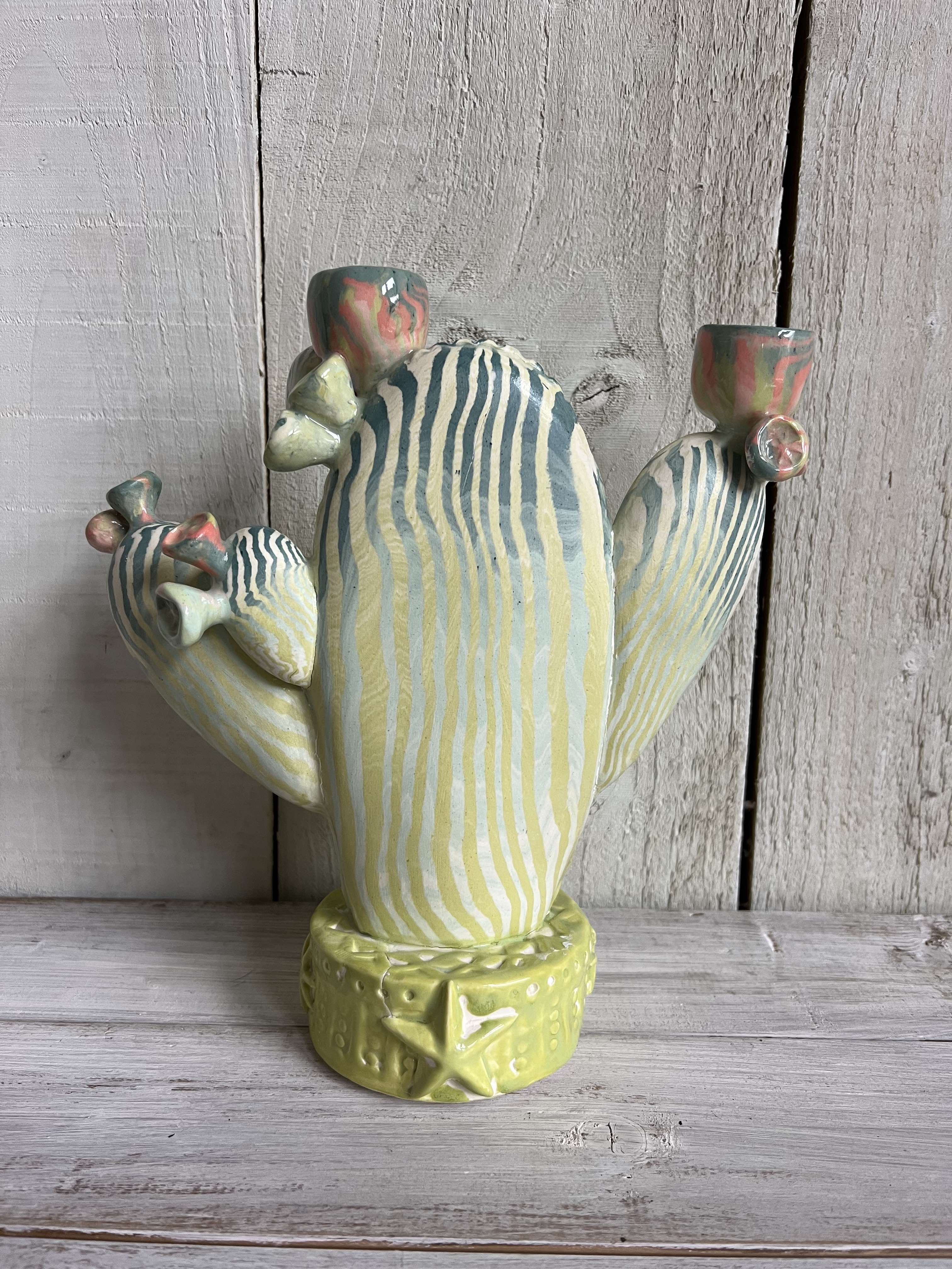 Handmade nerikomi ceramic cactus candle holder with striped clay pattern and coral flower details displayed on a rustic wooden shelf.