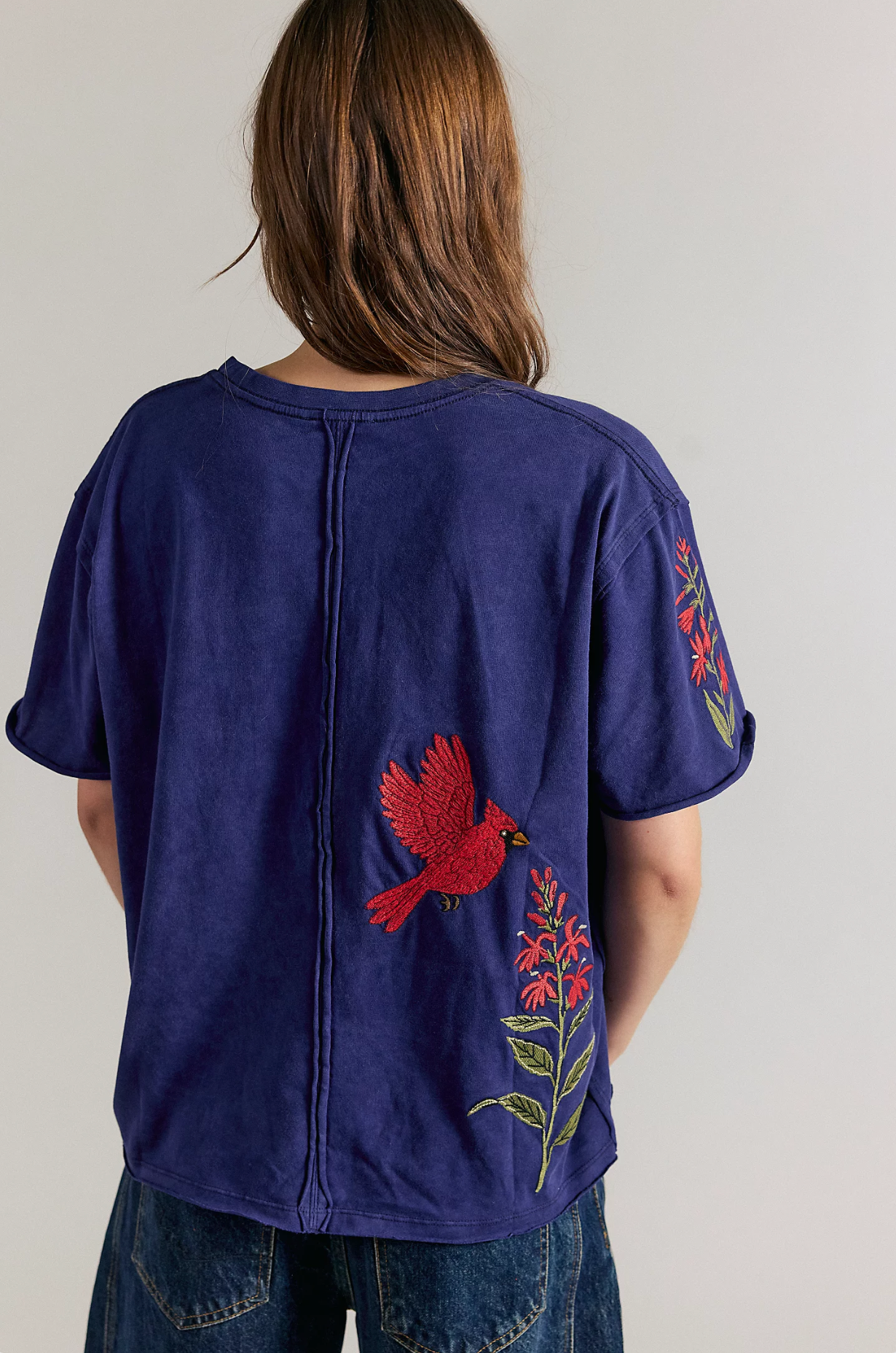 Back view of a person wearing a navy blue short-sleeve T-shirt featuring embroidered red cardinal birds on the lower hem.