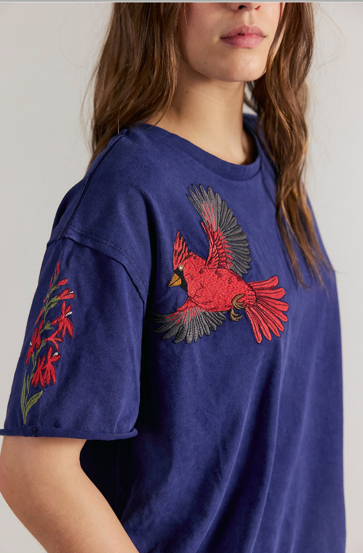 Side view of a person wearing a navy blue short-sleeve T-shirt featuring embroidered red cardinal birds on the shoulder and lower hem.