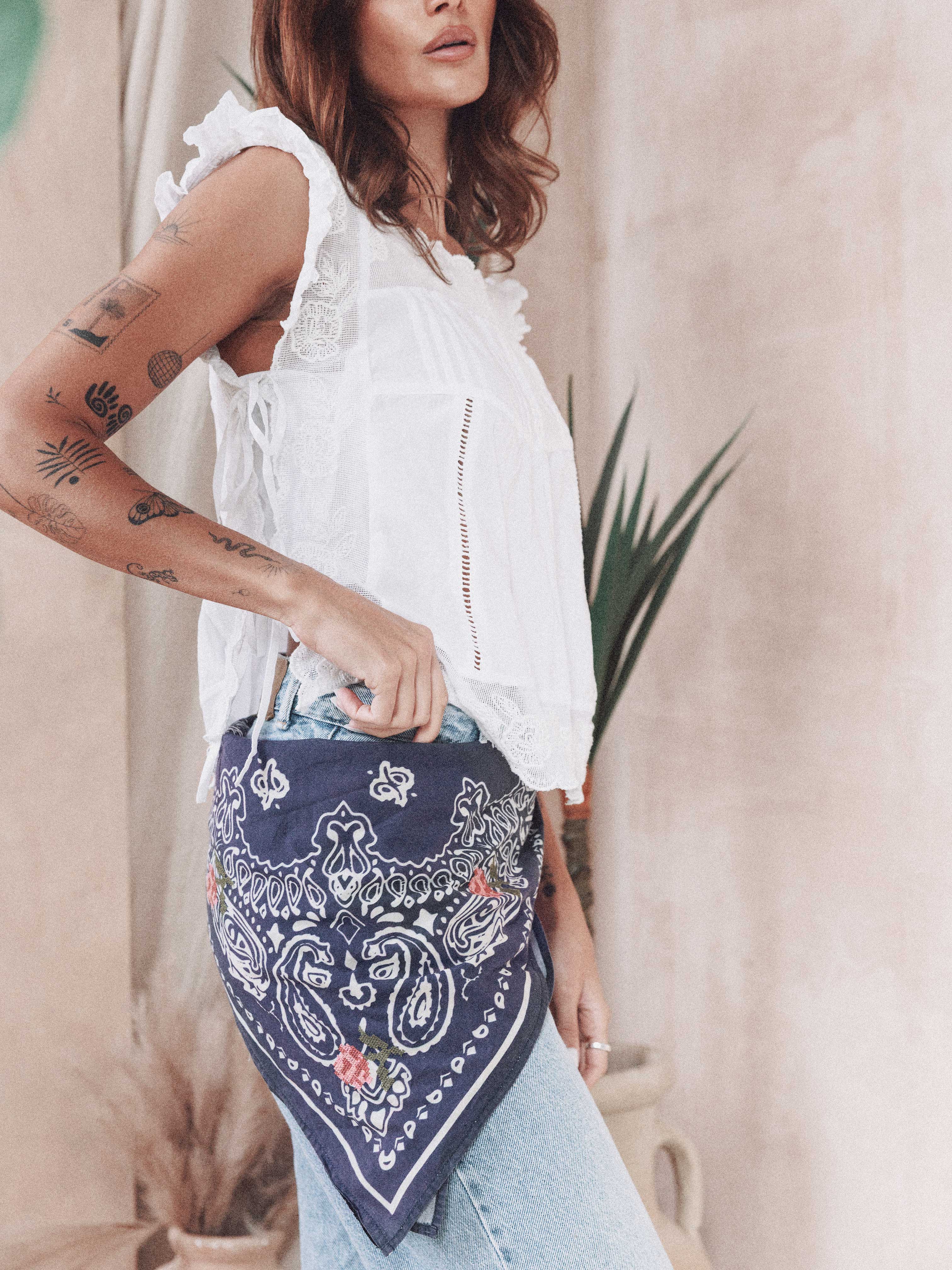 Woman styling a navy bandana print scarf with rose embroidery tied around her waist.