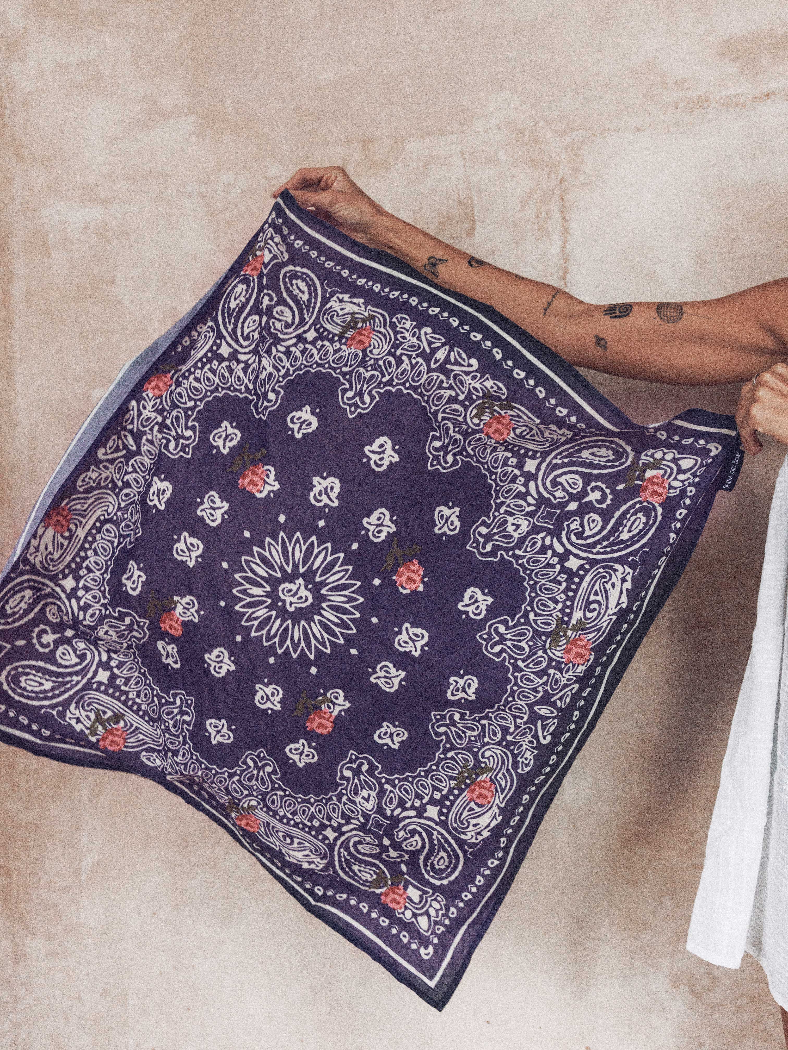 Person holding a navy bandana print scarf with rose embroidery and floral detailing.