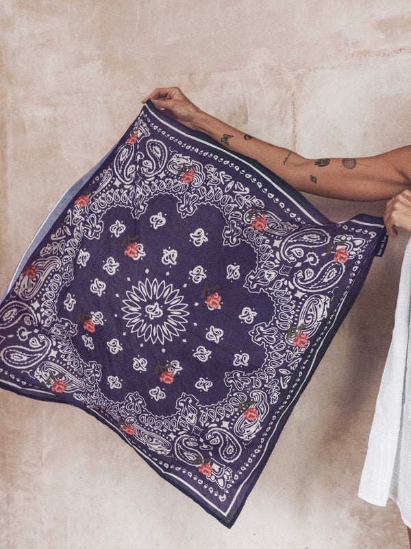 Person holding a navy bandana print scarf with rose embroidery and floral detailing.