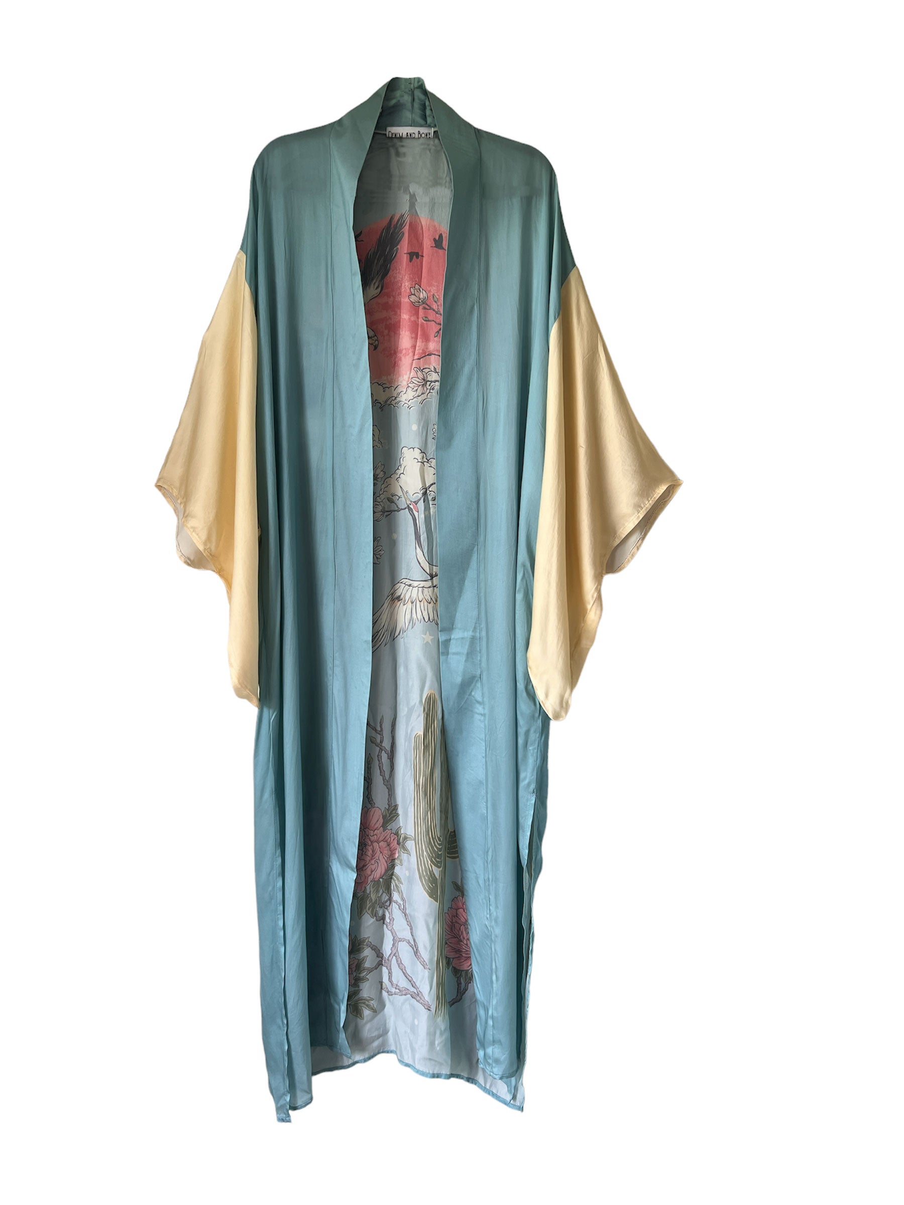 A sky blue kimono with intricate crane, moon, eagle, and cactus designs in gold and red.