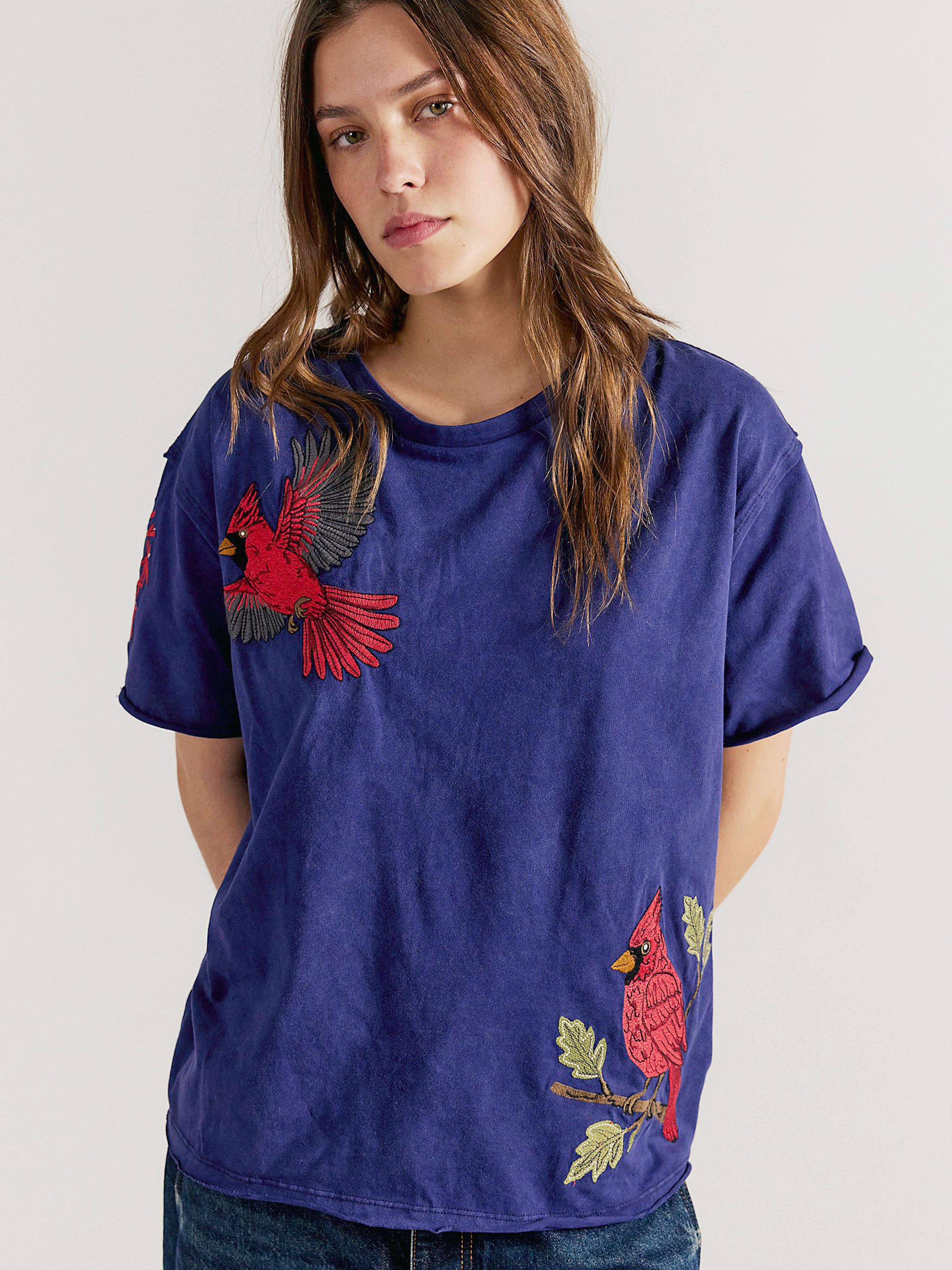 Front view of a person wearing a navy blue short-sleeve T-shirt featuring embroidered red cardinal birds on the shoulder and lower hem.