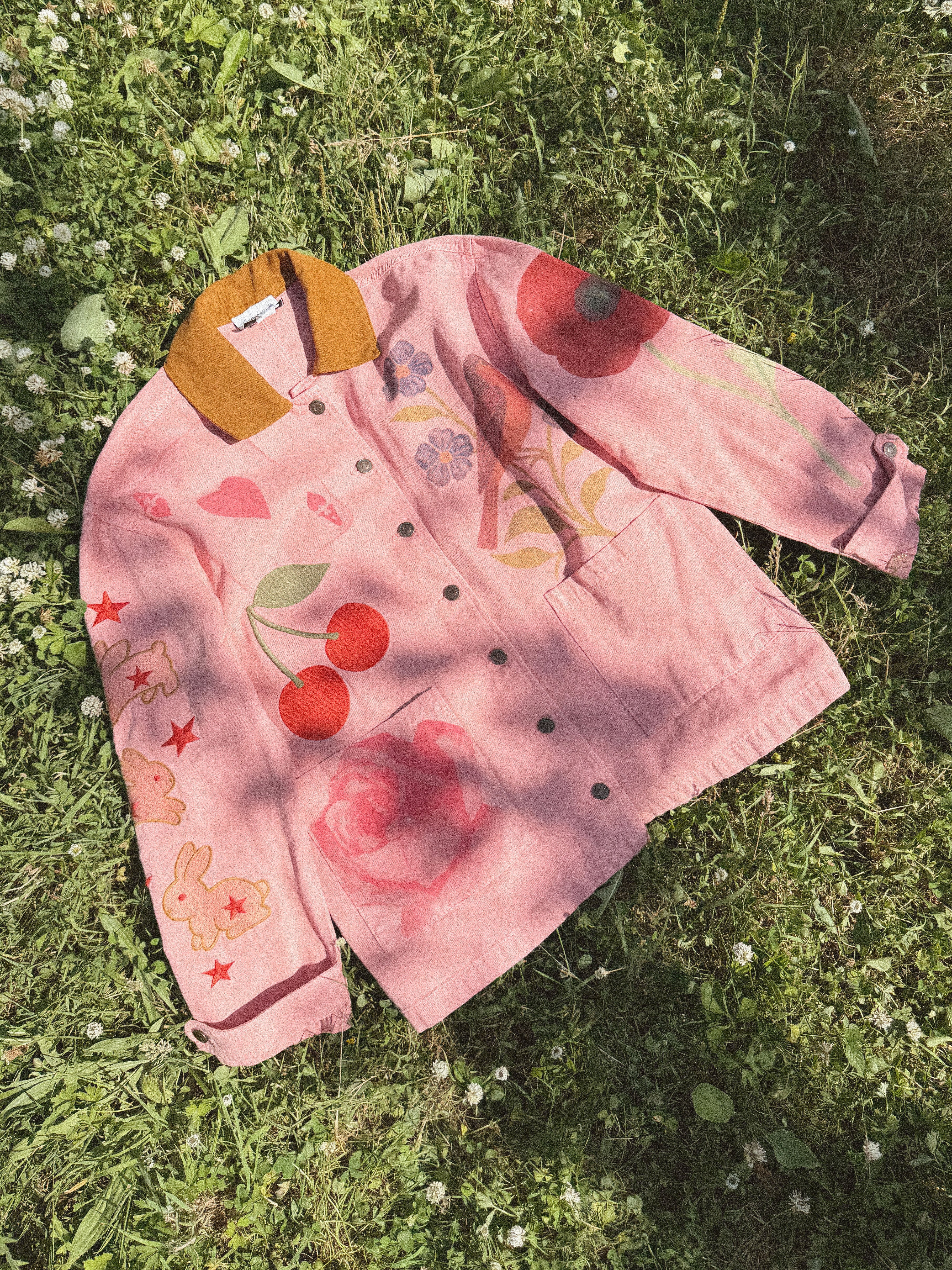 Front view of a pink women's jacket with colourful hand-painted cherries, flowers, hearts, stars, and bunny illustrations.