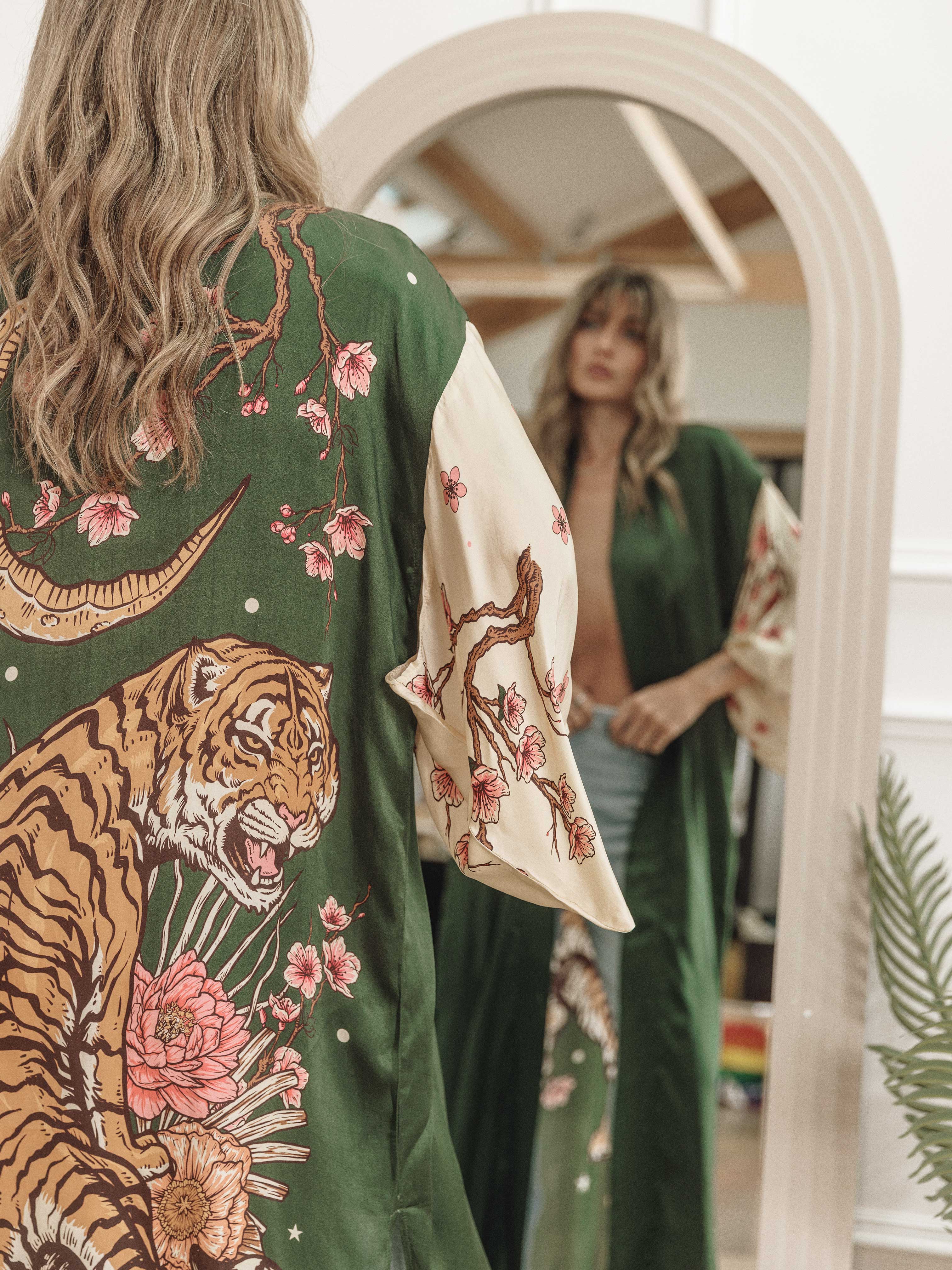 Back view of a dark green kimono-style cardigan featuring a tiger, crescent moon, and floral print, reflected in a mirror.