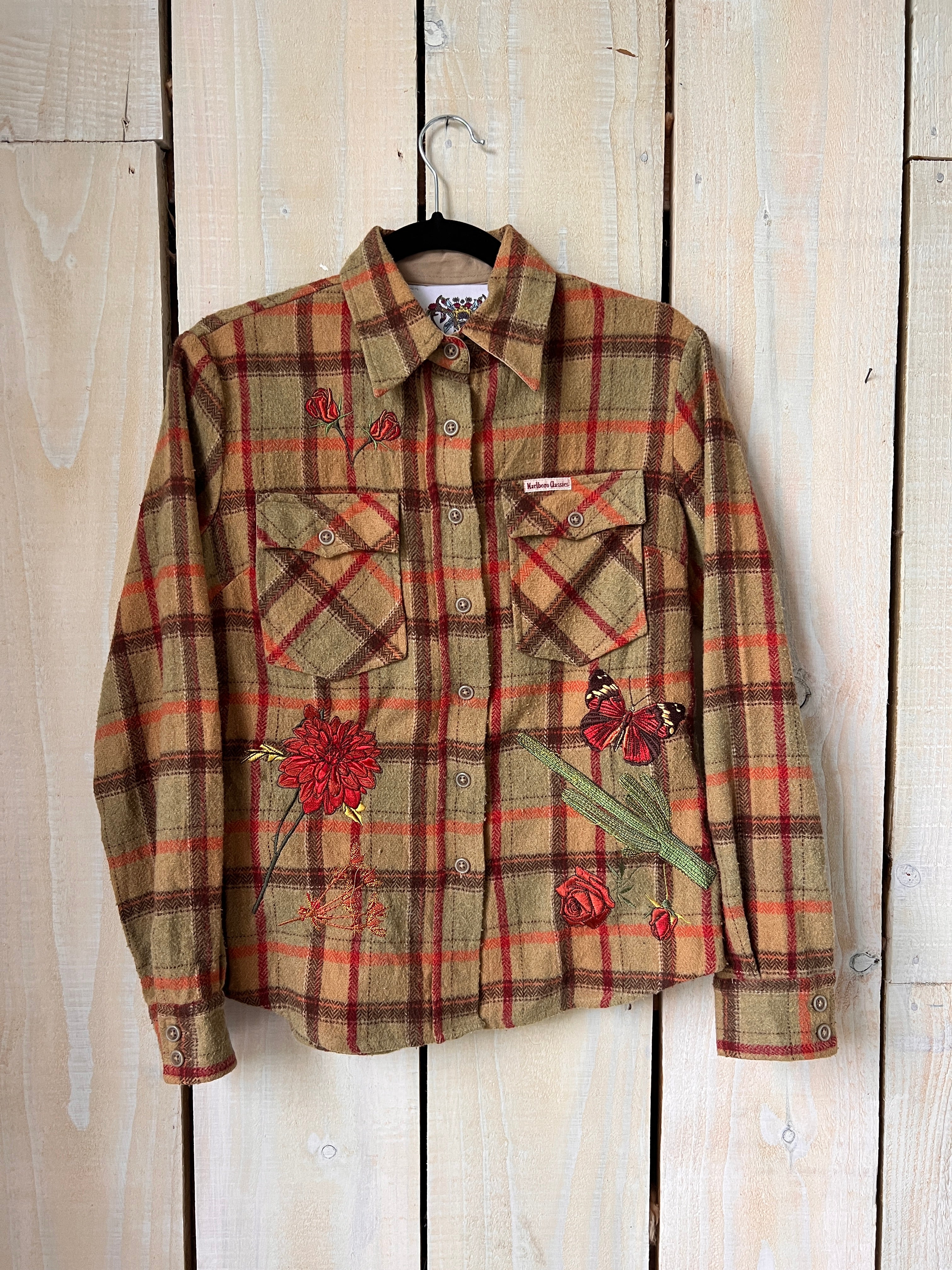 Tan plaid shirt with red floral embroidery on the front.