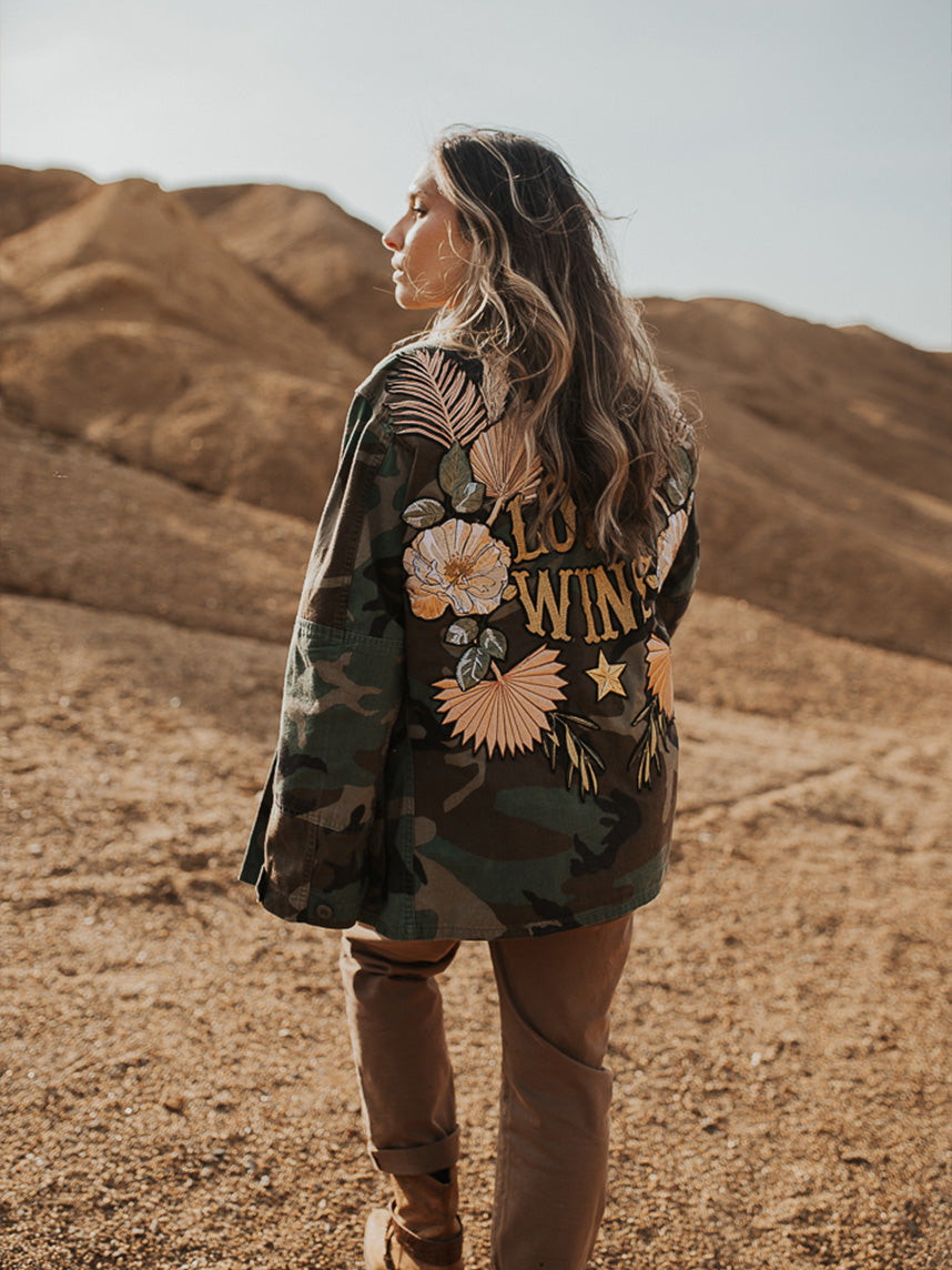 Camouflage jacket with floral embroidered back design and "LOVE WINS" lettering, shown from the back.
