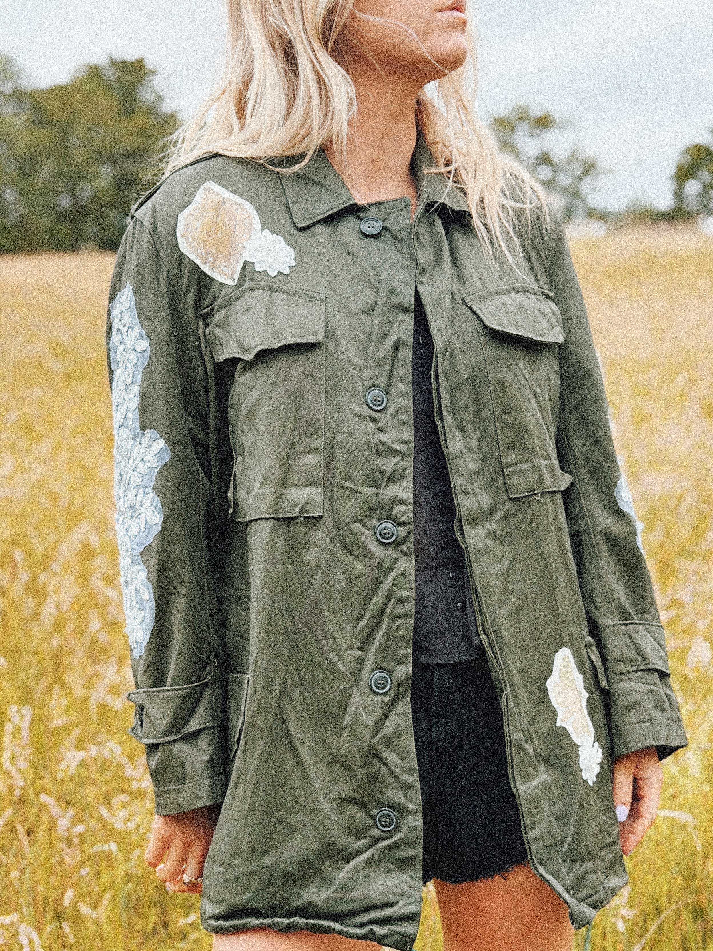 Olive green military jacket with white floral lace appliqué on the front and sleeves, front view.
