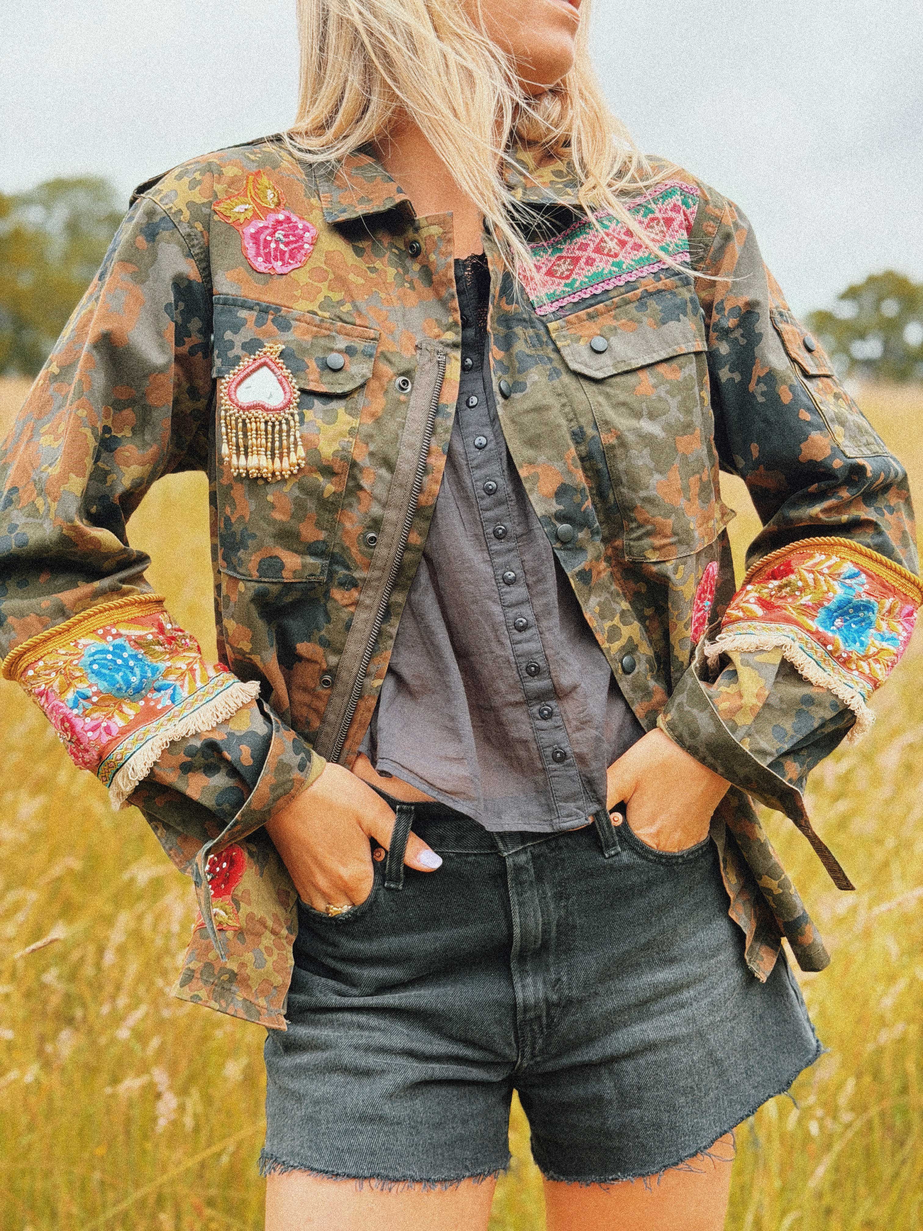 Embellished camouflage jacket with embroidered shoulder panel, decorative chest patch, and embroidered sleeve cuffs, front view.