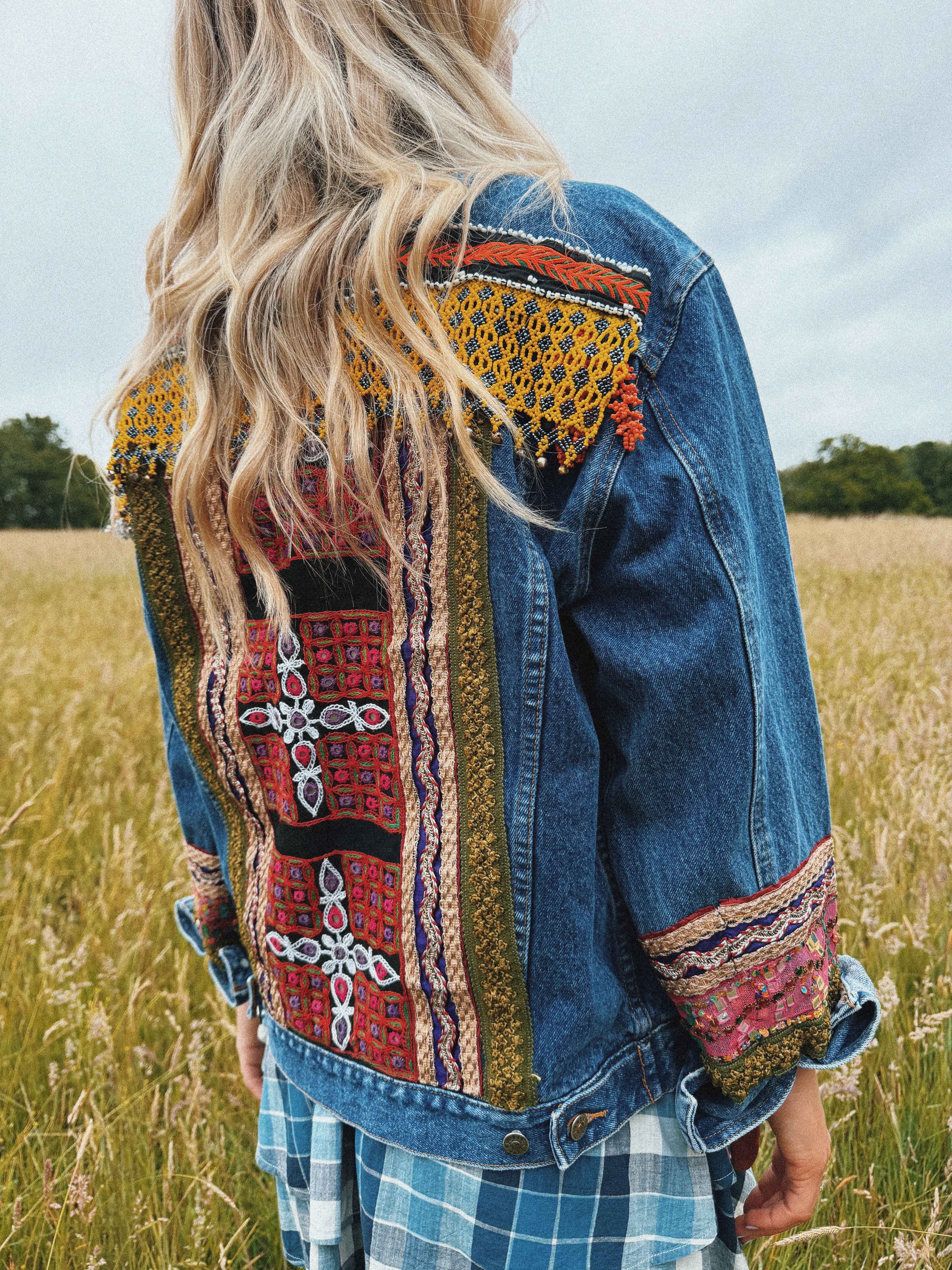Dark blue denim jacket featuring a colourful embroidered back panel and decorative sleeve cuffs.