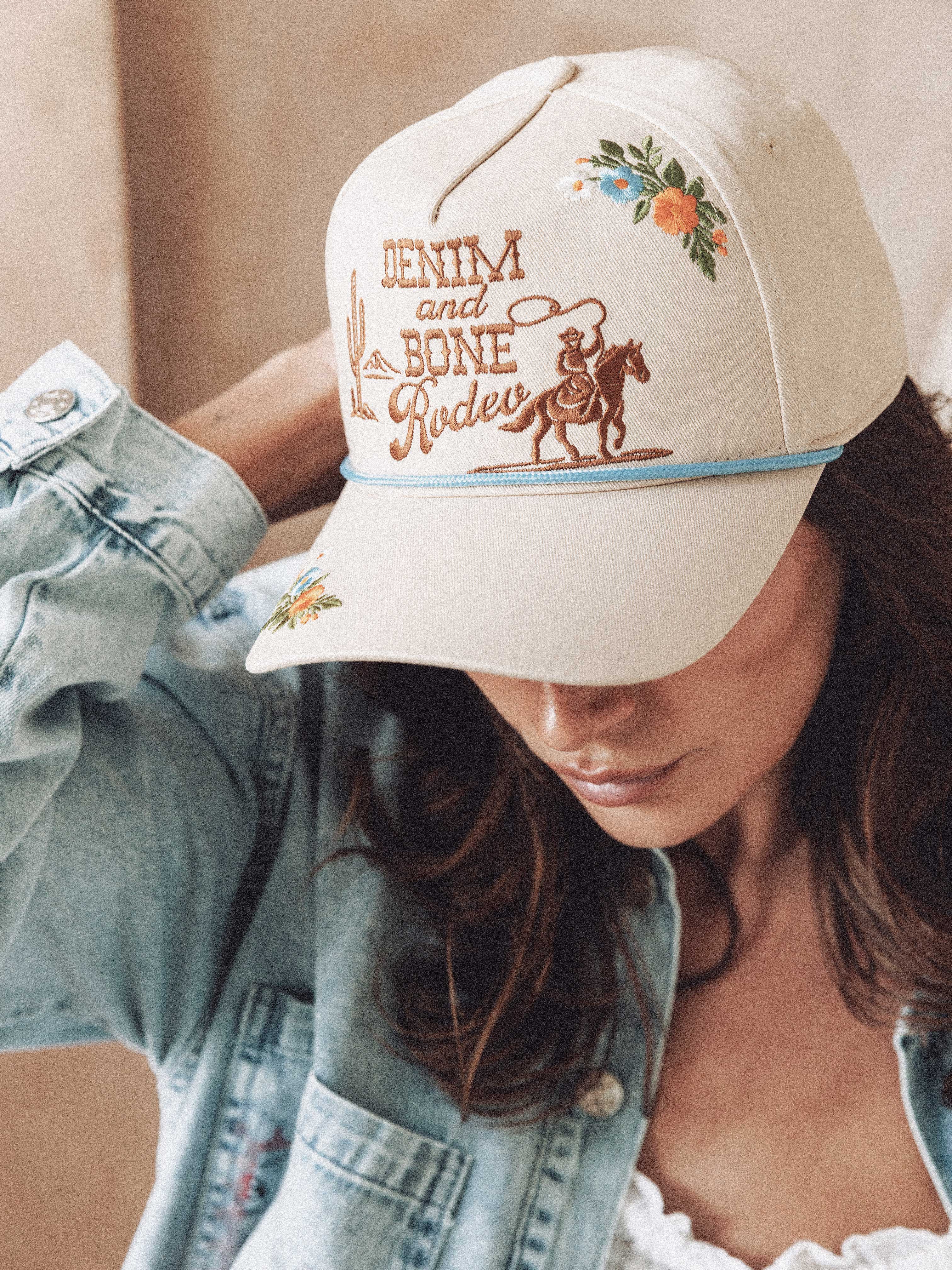 Woman wearing a cream "Denim and Bone Rodeo" embroidered baseball cap with floral and cowboy details.