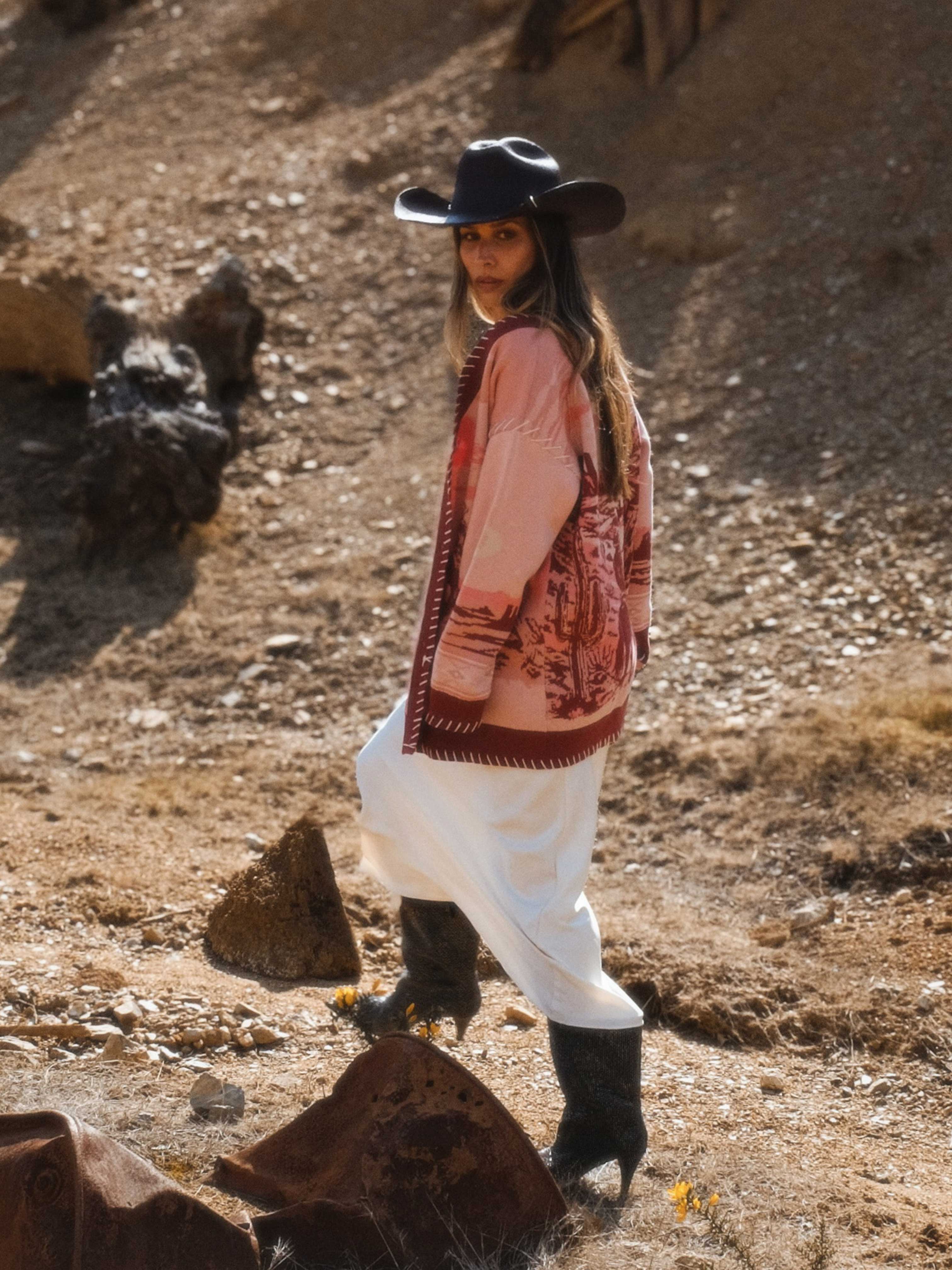 Person wearing a pink knit cardigan with a western desert landscape knit pattern featuring horses and riders.
