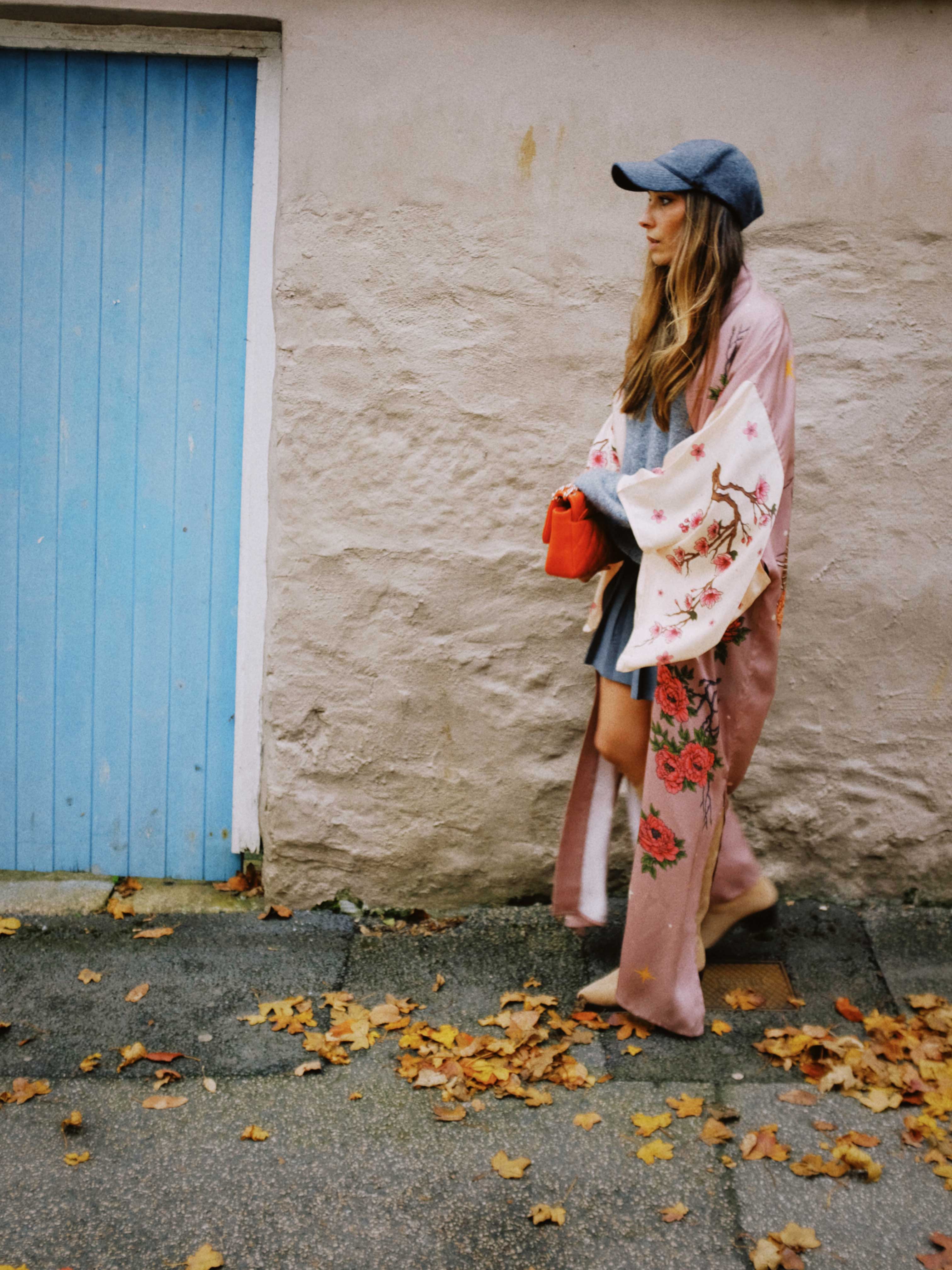 Person wearing a long pink kimono-style robe with cherry blossom branches and floral print over a blue dress while walking outdoors.
