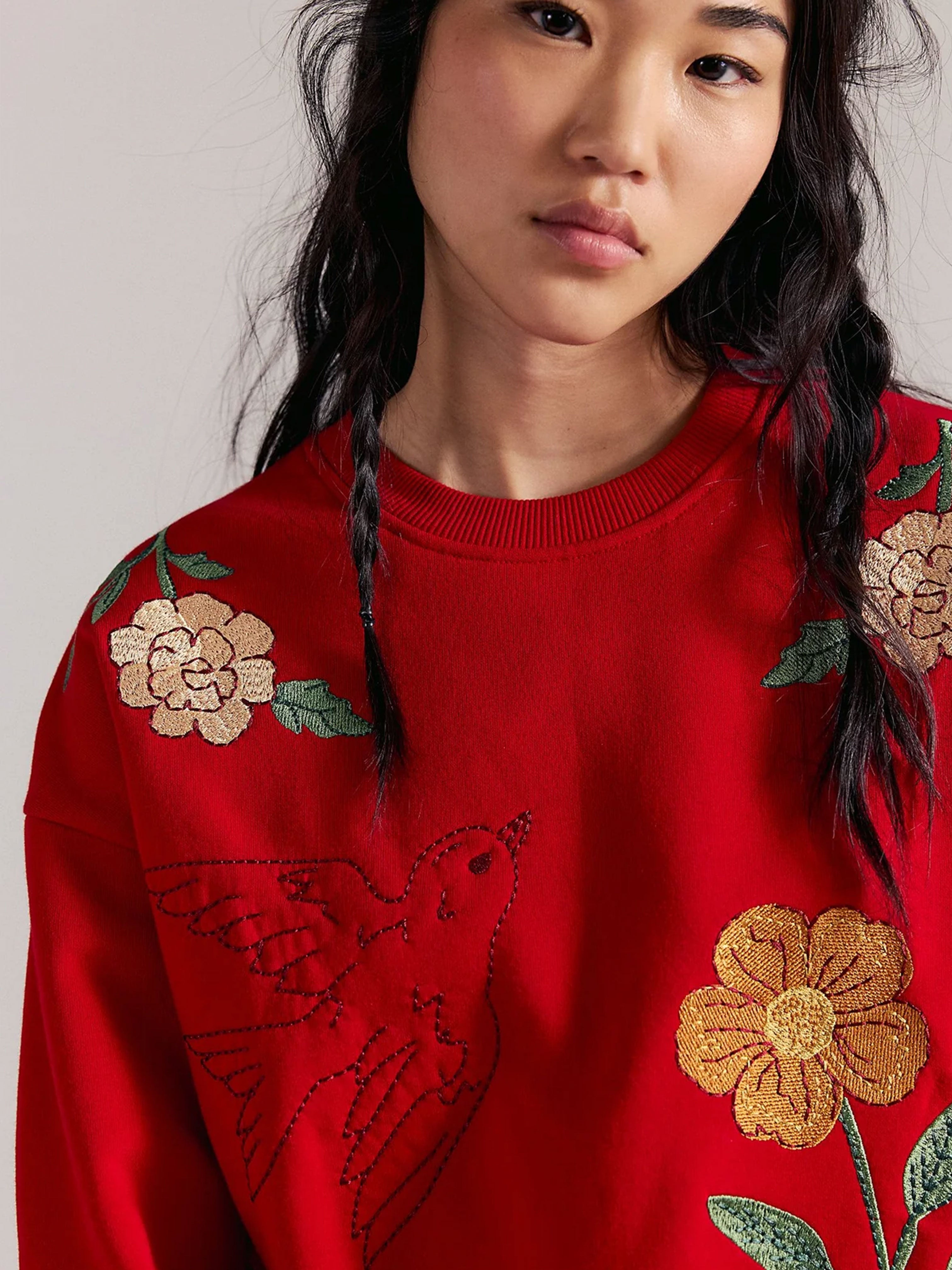 Woman wearing a red sweatshirt with embroidered flowers and a swallow on the front.