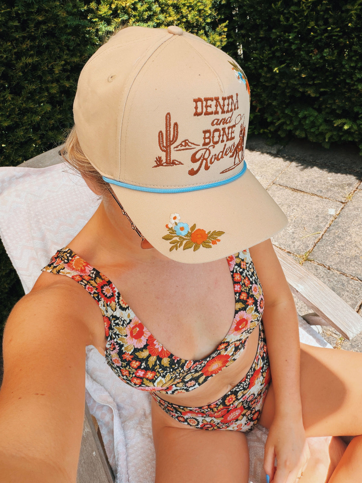 Woman wearing a cream "Denim and Bone Rodeo" embroidered baseball cap by the pool.