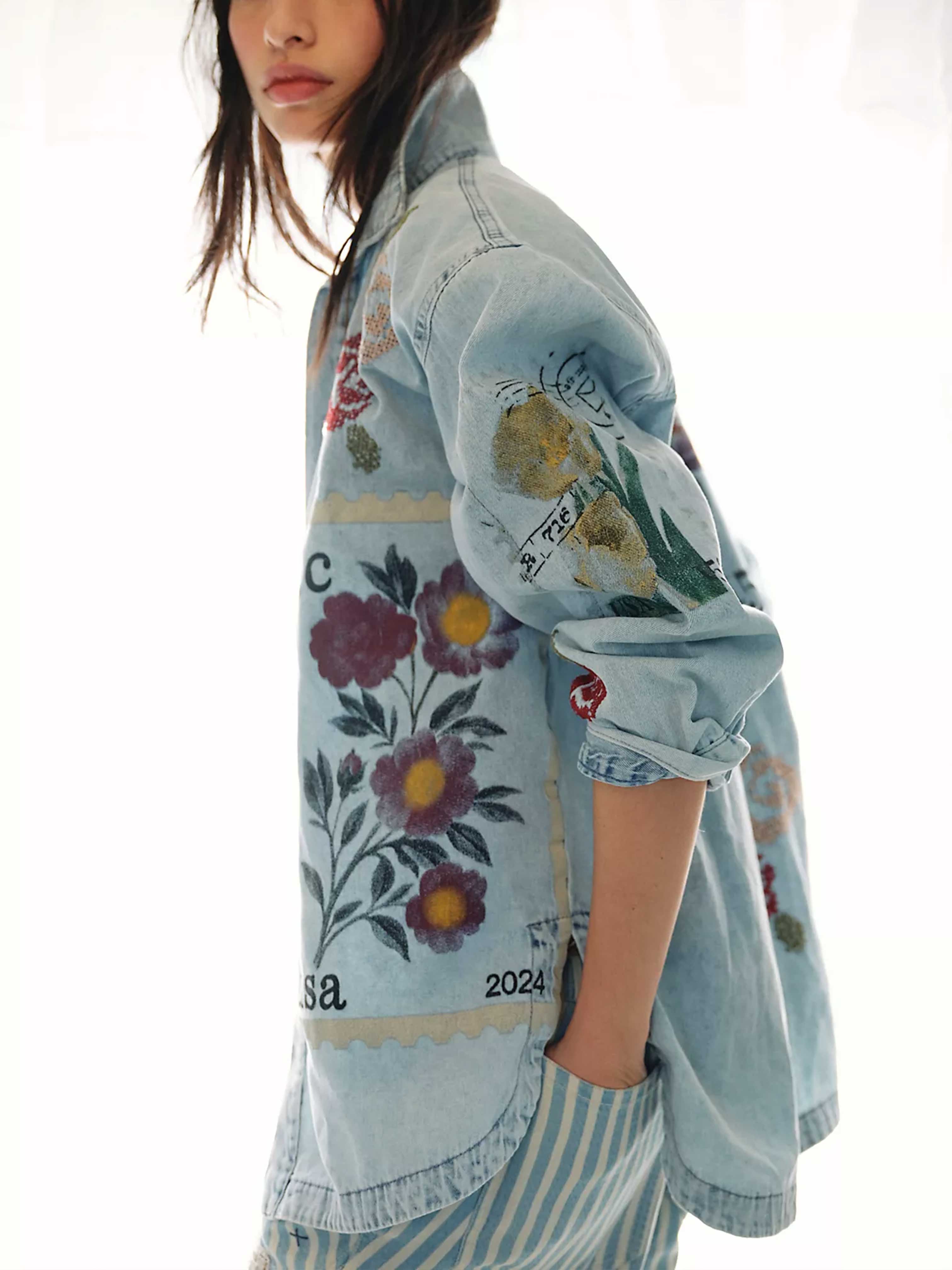 Side view of a person wearing a light wash denim button-up shirt featuring vintage-inspired postage stamp patchwork with floral cross-stitch artwork, paired with blue and white striped pants.
