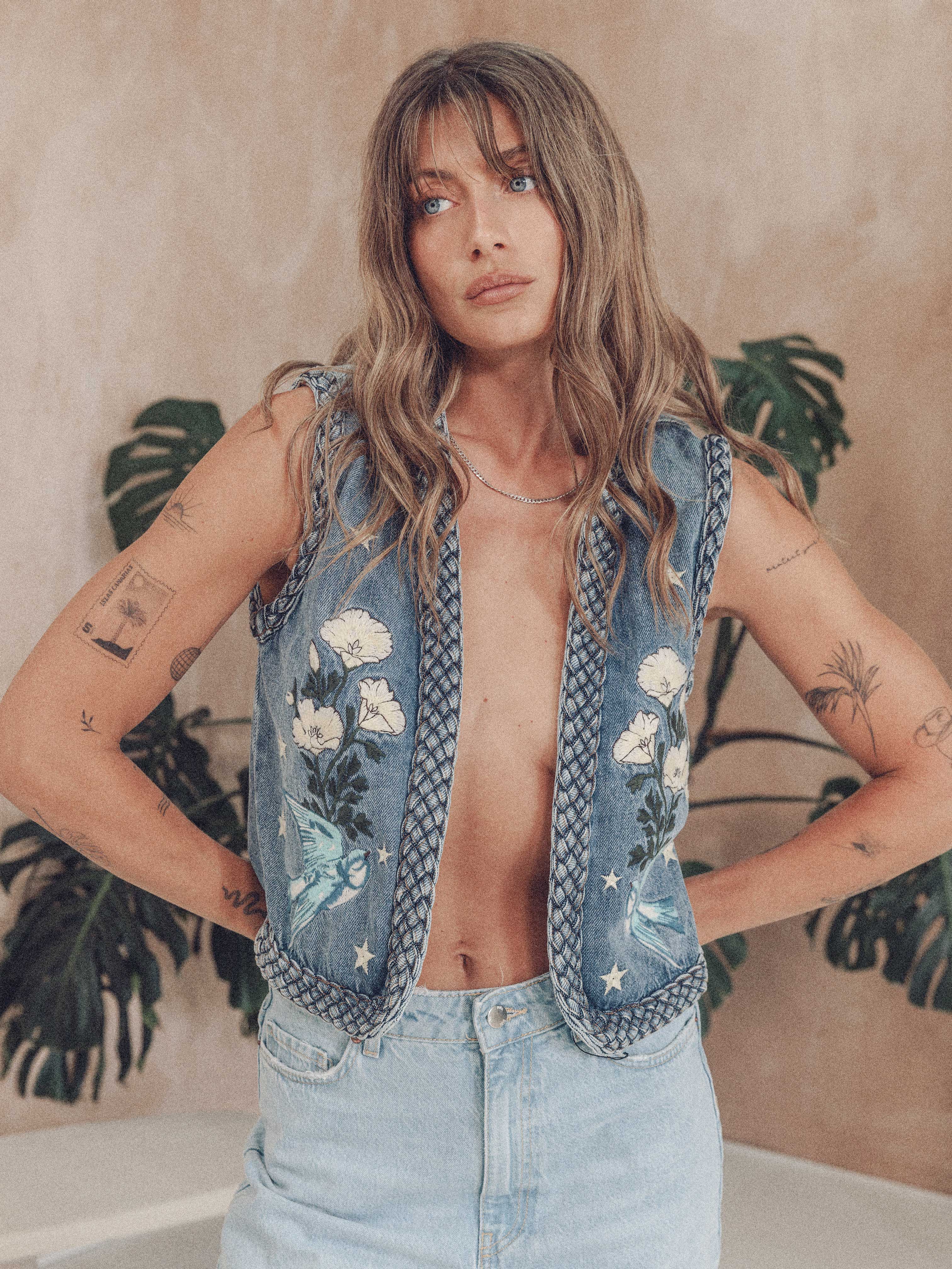 Front view of a person wearing a blue denim vest with white florals, birds and star embroidery details