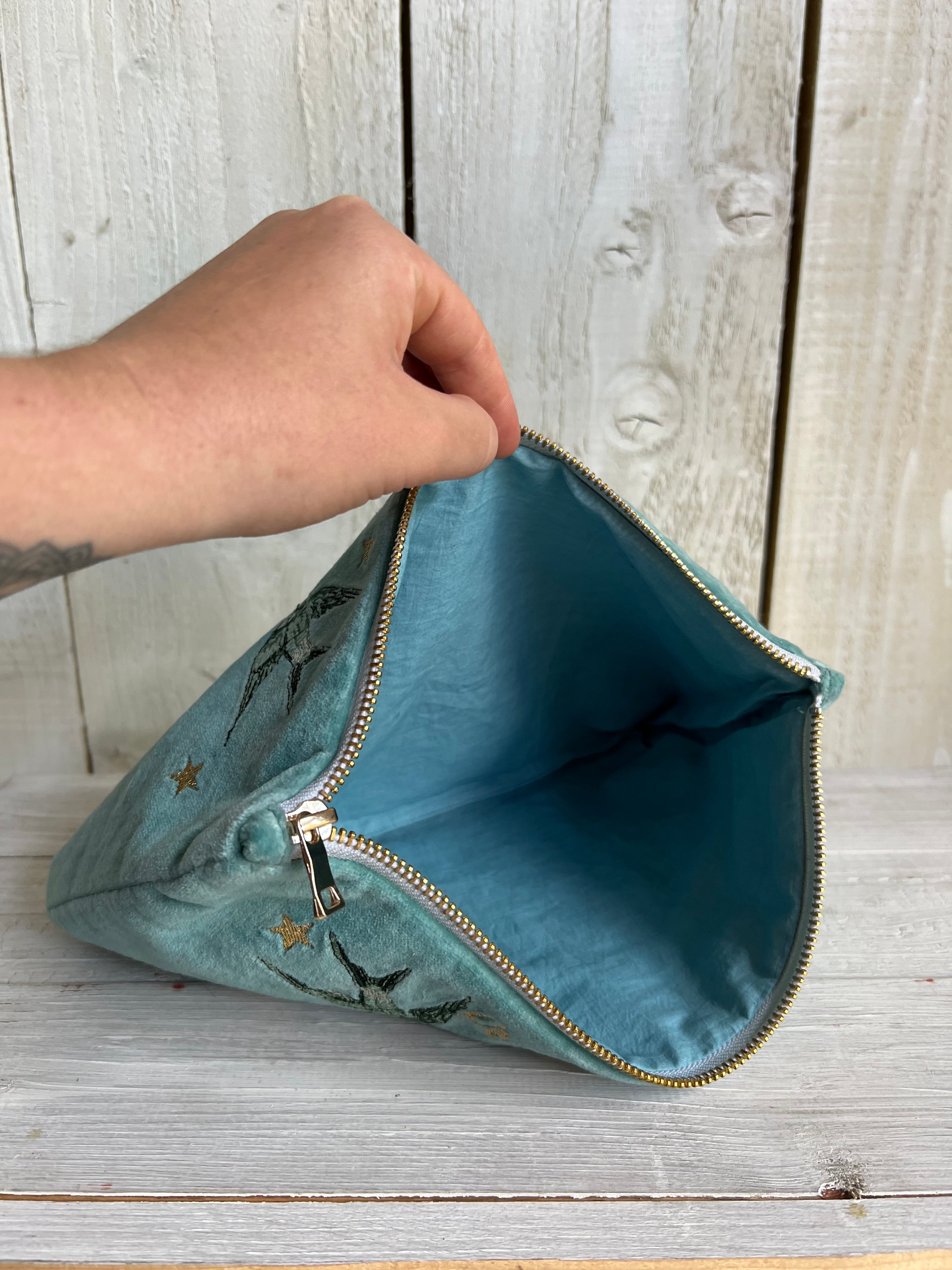 Open turquoise velvet zip pouch showing the spacious lined interior and gold-tone zip closure.
