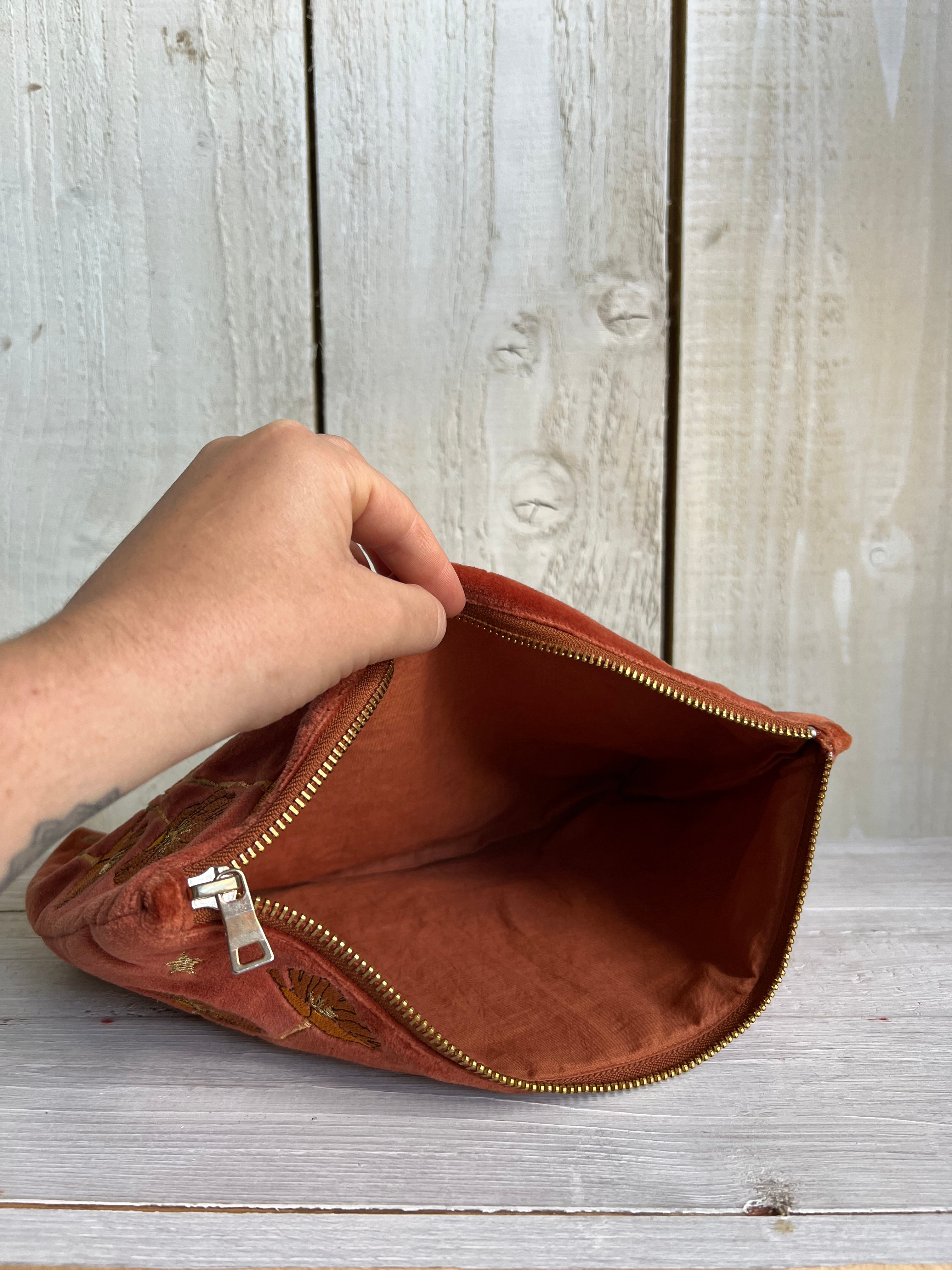 Open rich rust velvet zip pouch showing the spacious lined interior and gold-tone zip closure.