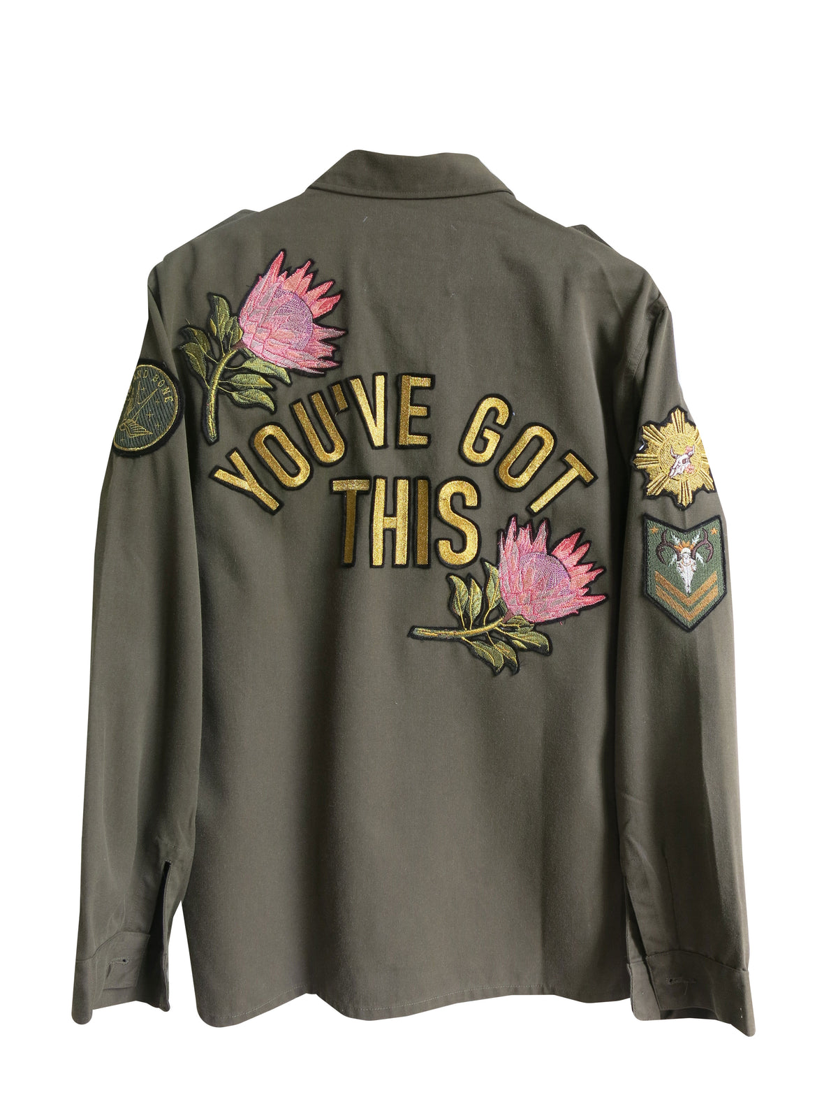 Back view of an olive green military jacket with embroidered "YOU'VE GOT THIS" lettering, pink protea flower embroidery, and military-inspired sleeve patches.