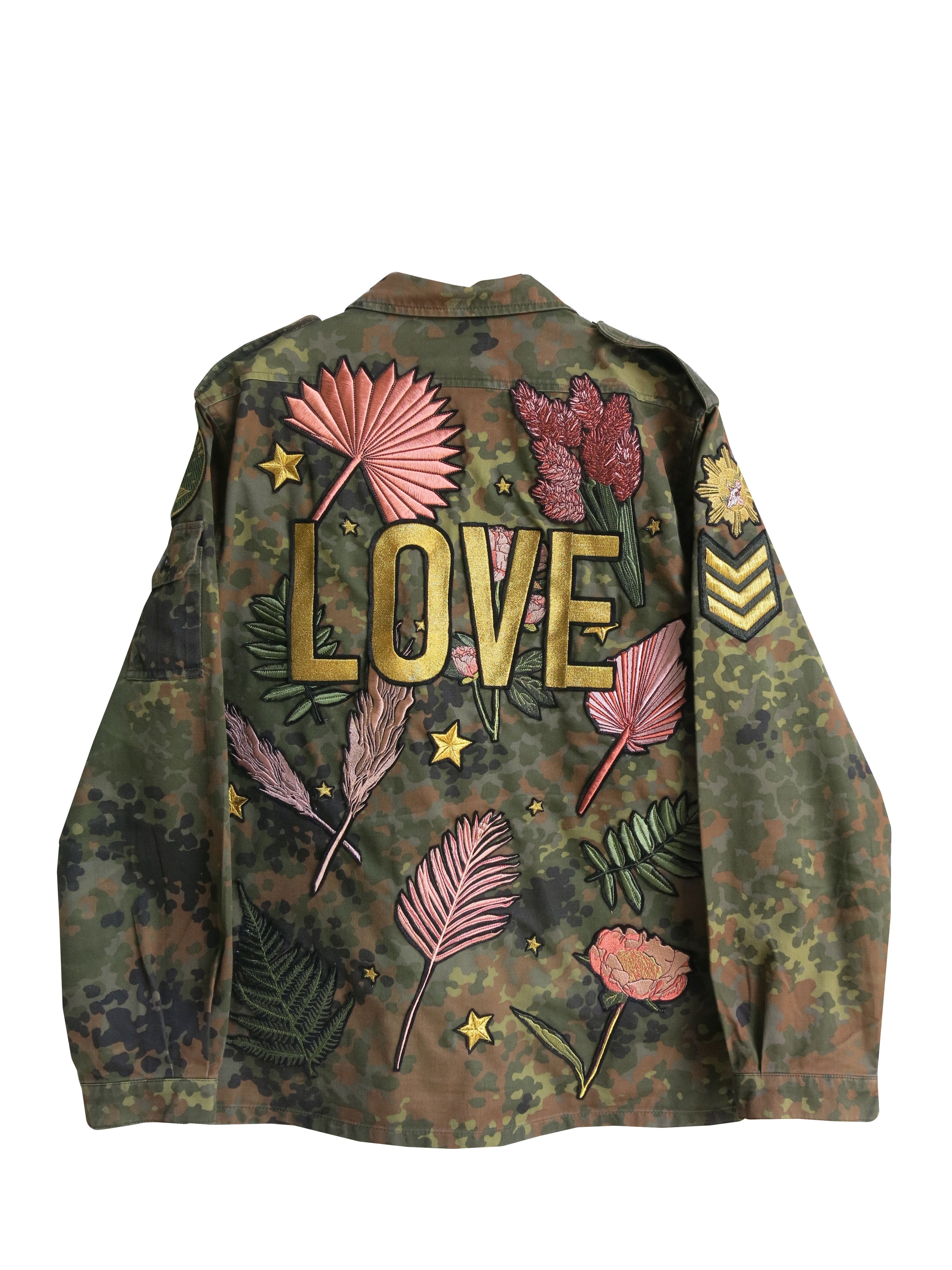 Back view of a camouflage military jacket with large "LOVE" embroidery, botanical embroidery, and decorative military-inspired sleeve patch.