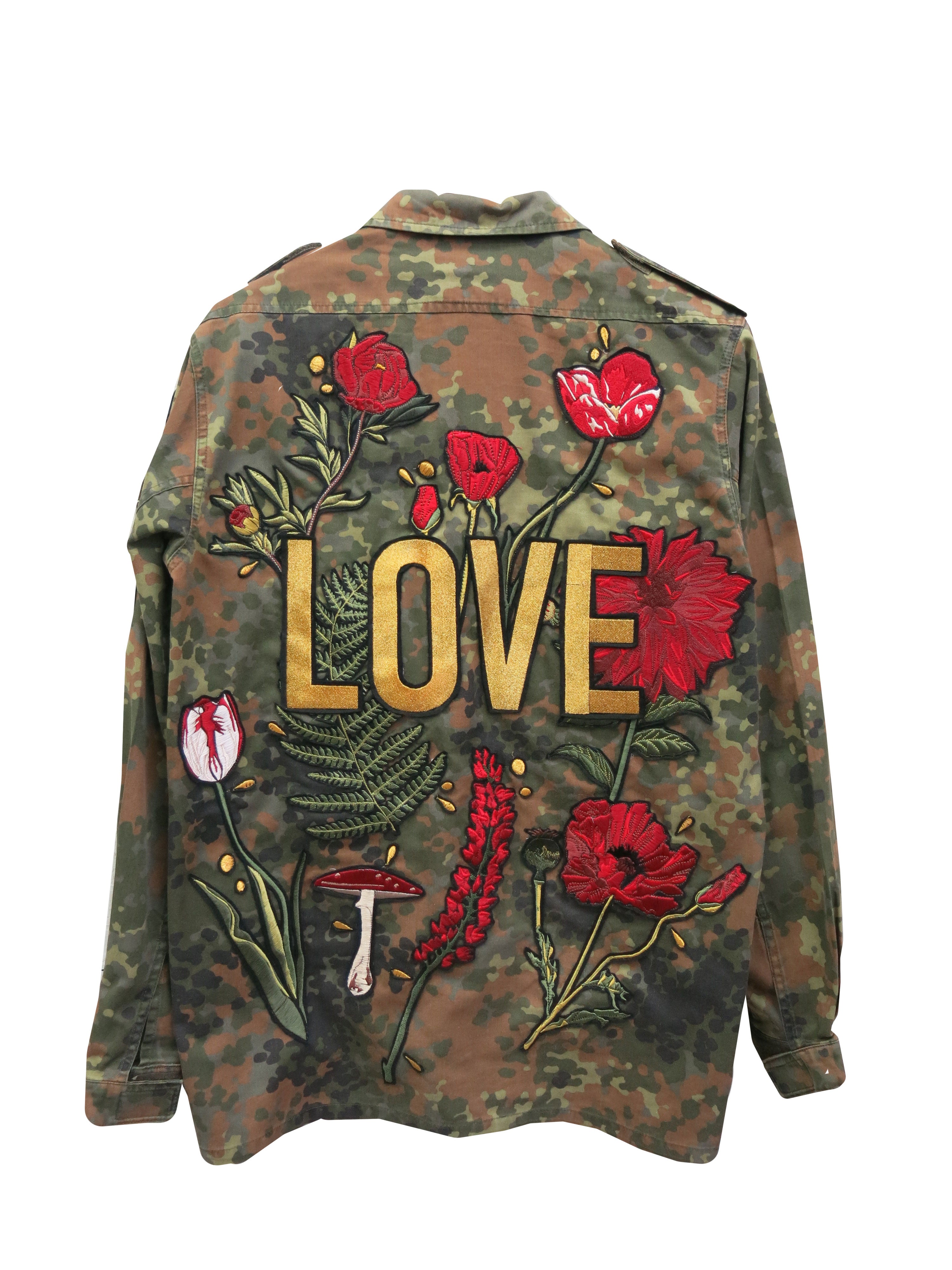 A camouflage military jacket with a large embroidered "LOVE" design surrounded by red flowers and botanical motifs.