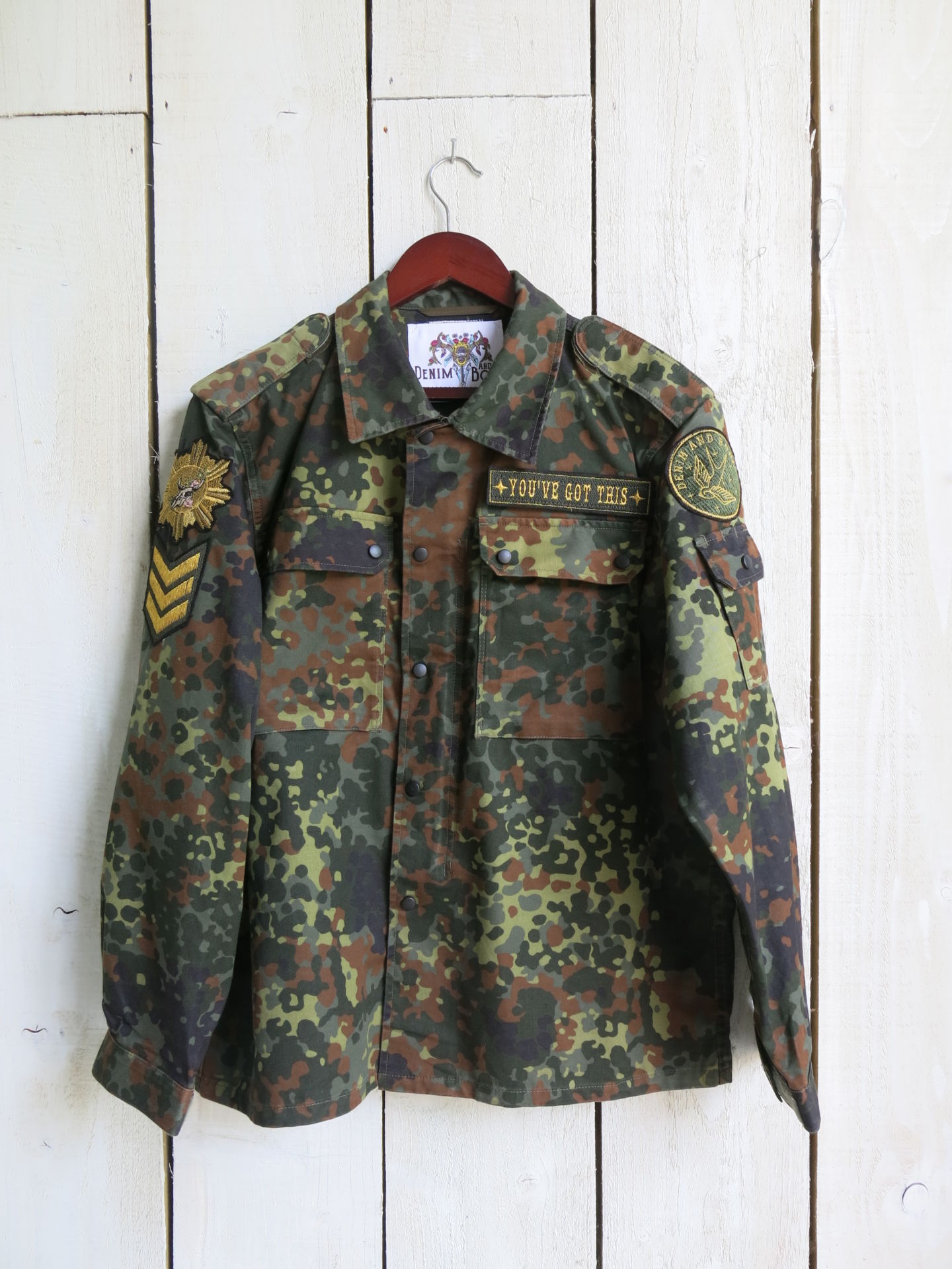Front view of a camouflage military jacket with military-inspired patches and a "YOU'VE GOT THIS" embroidered chest patch.
