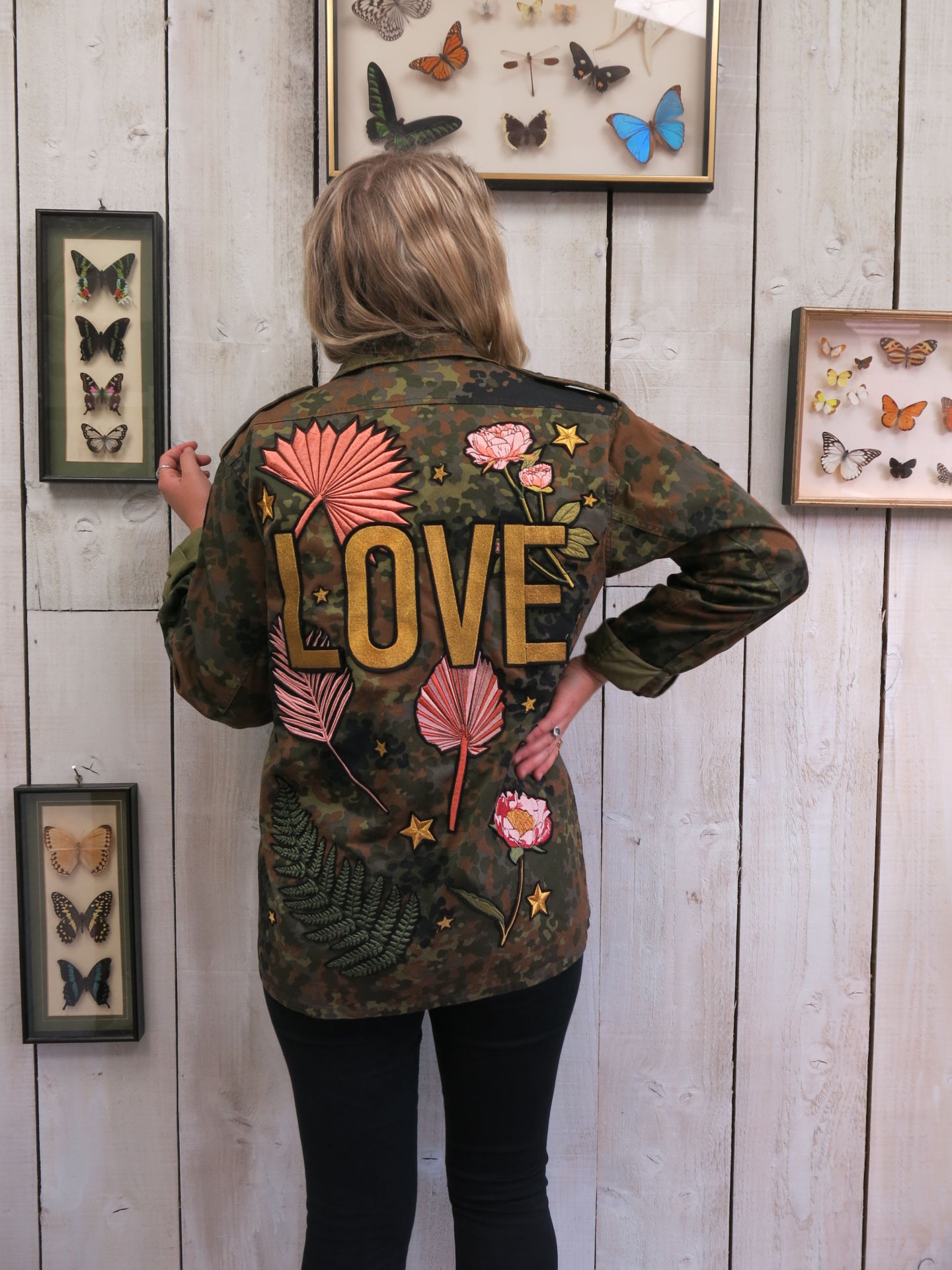 Camouflage military jacket with "LOVE" embroidered back design and floral embroidery, shown from the back.