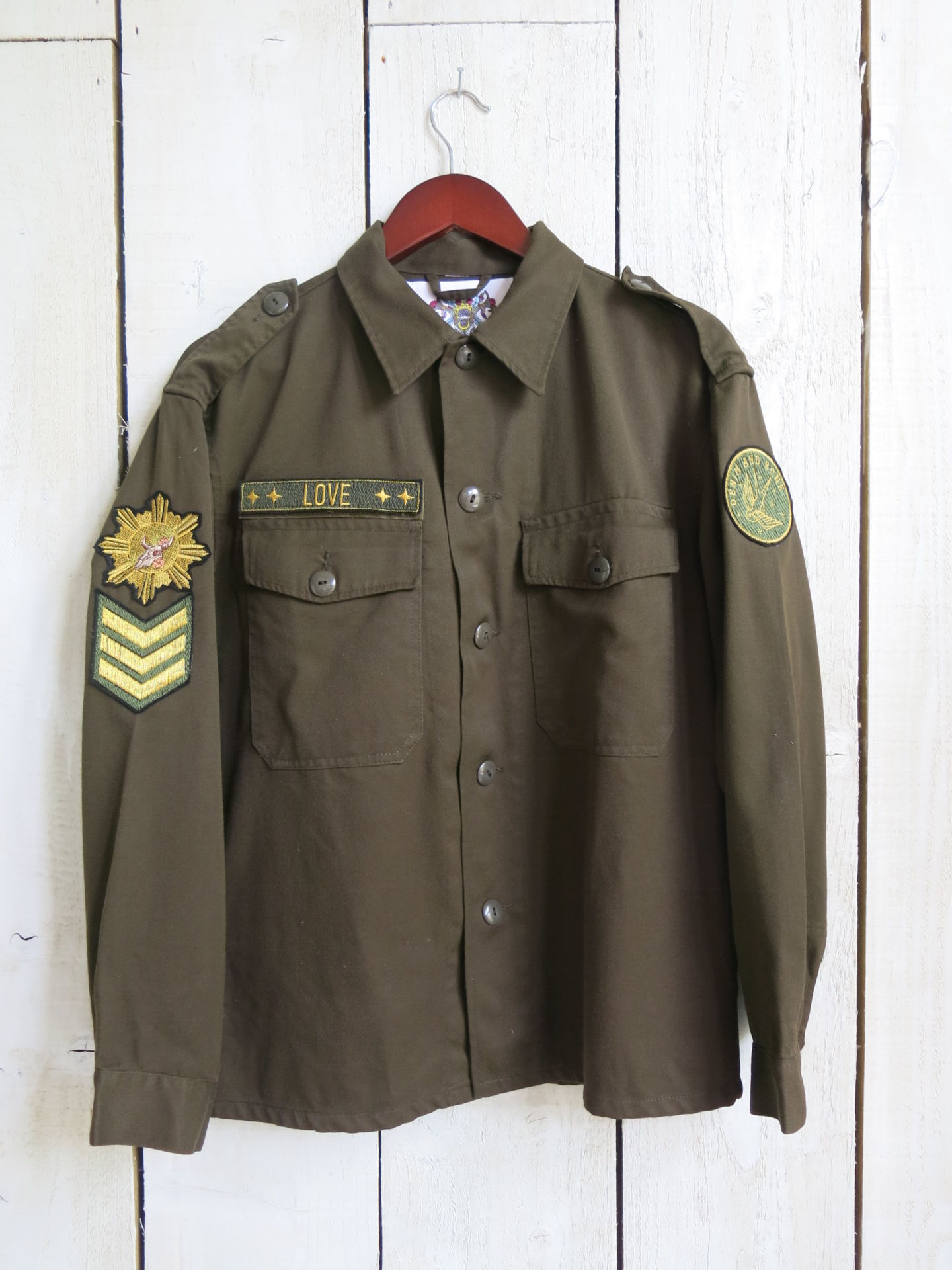 Olive green military jacket with decorative patches and "LOVE" chest embroidery, front view.